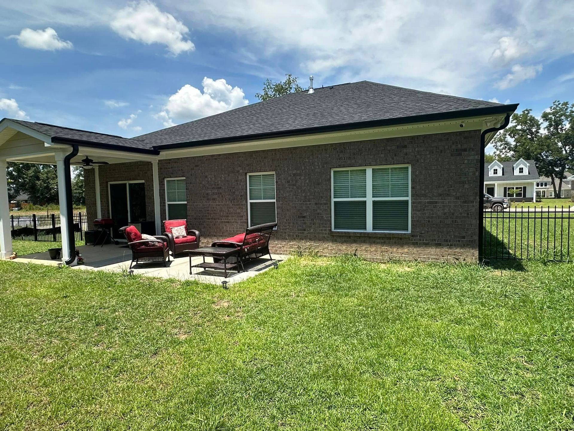 Backyard patio with red chairs beside a brick house and large grassy lawn under a blue sky