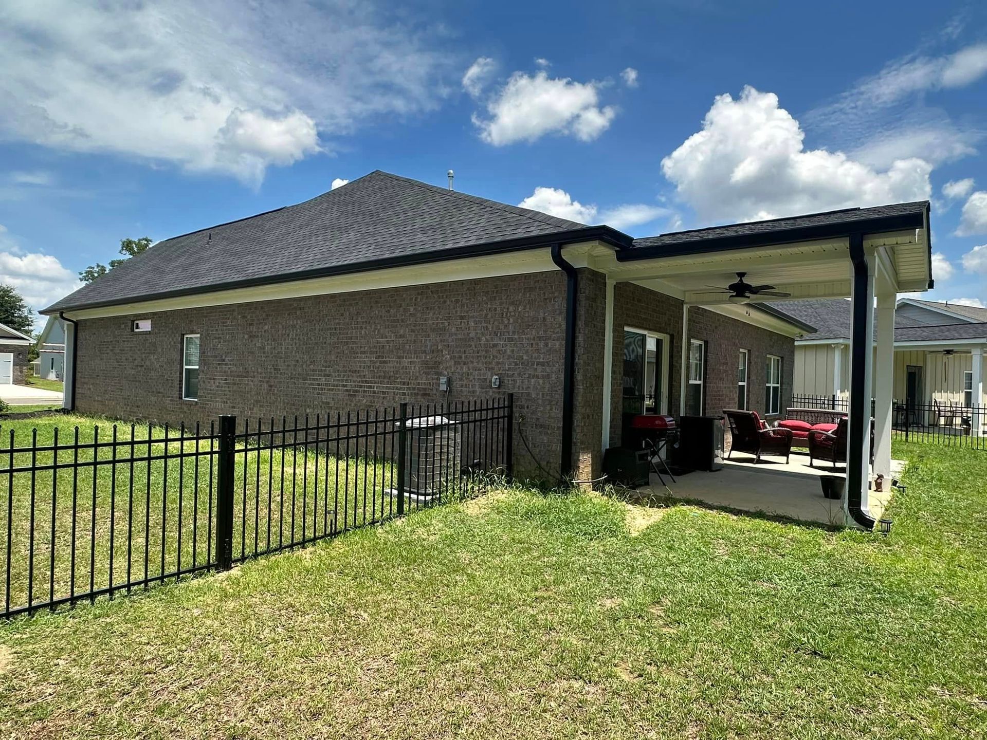 Brick house with a black metal fence and a covered carport under a cloudy blue sky