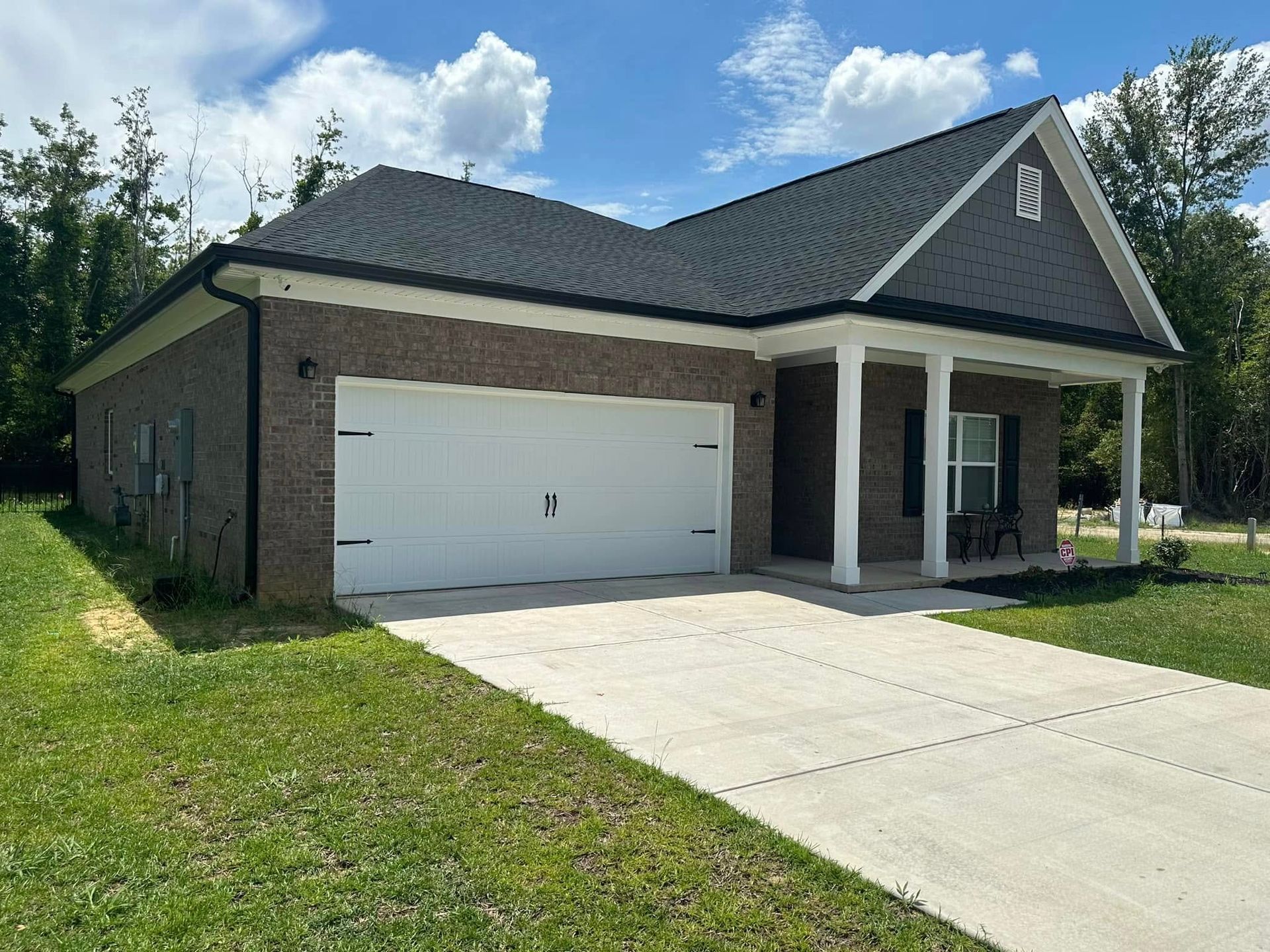Suburban house with a white garage door, covered porch, and concrete driveway under a partly cloudy sky