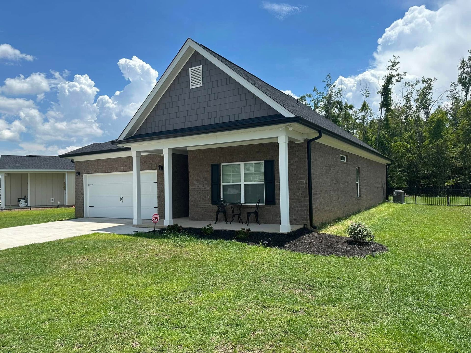Single-story brick house with a front porch, white garage, and green lawn under a blue sky