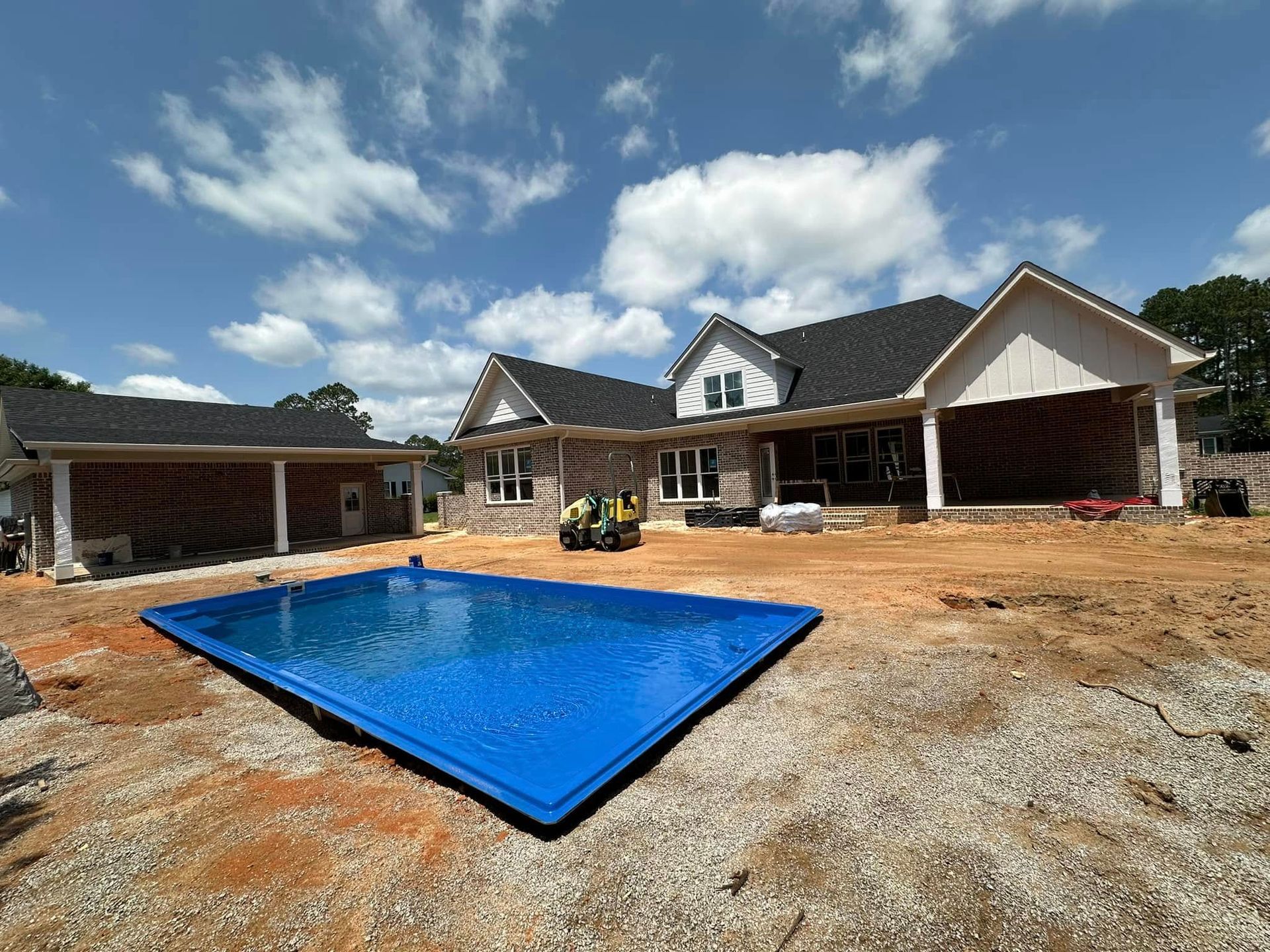 House under construction with a blue swimming pool in the foreground and dirt lot around it
