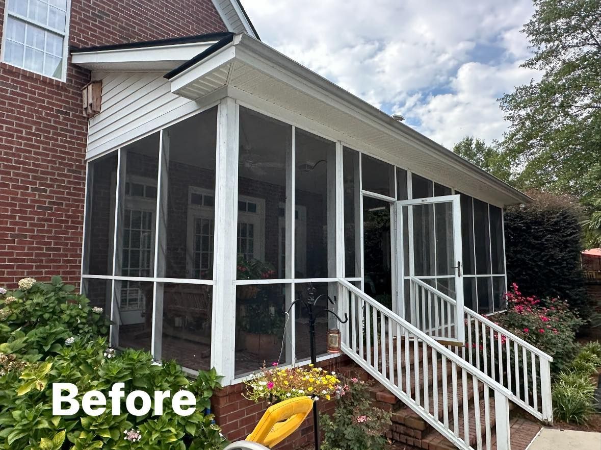 Enclosed porch with white screened windows, railing, brick wall, and flowers in front of a house.
