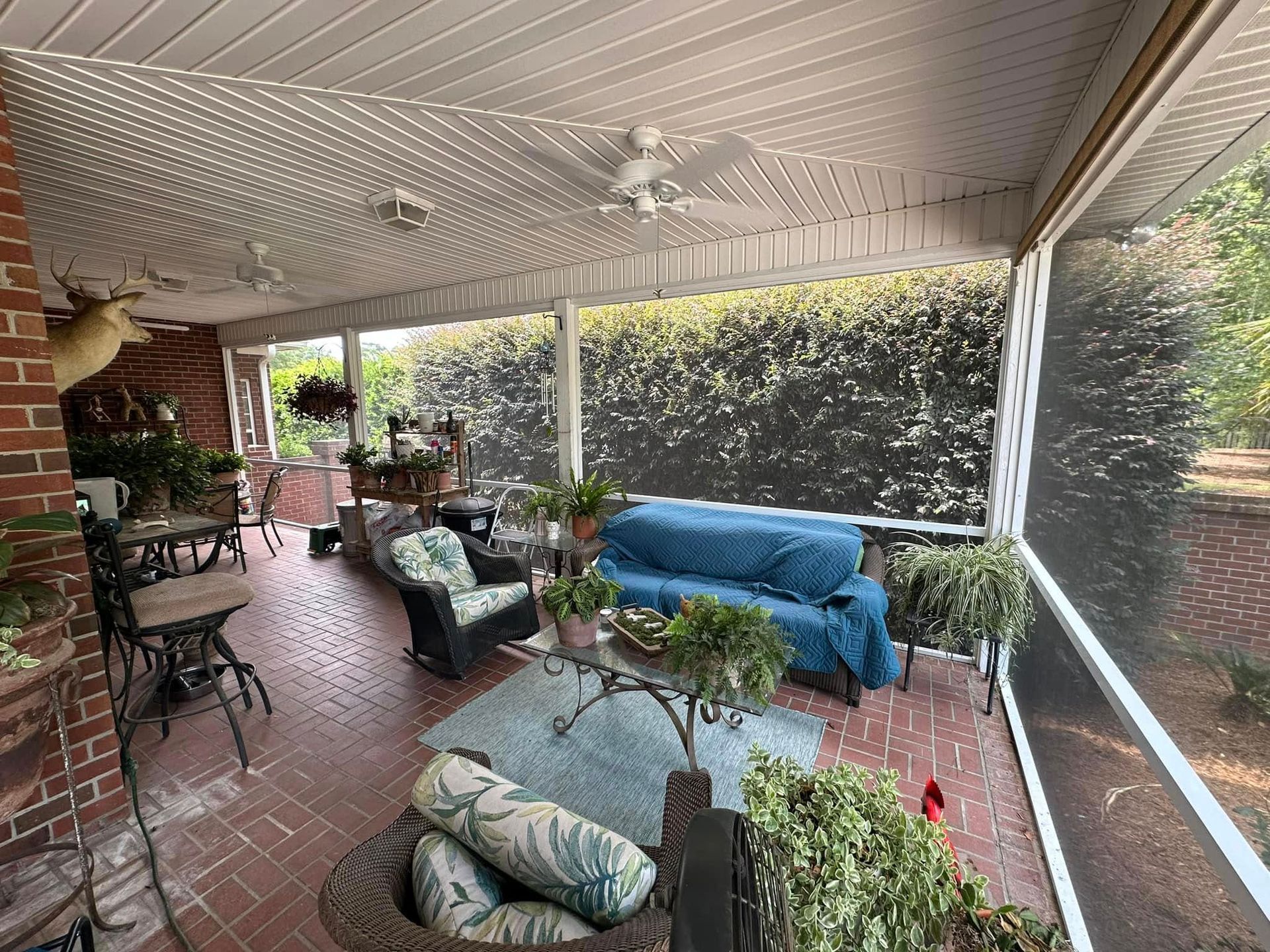 Covered patio with brick floor, outdoor seating, potted plants, and a blue loveseat behind screened walls