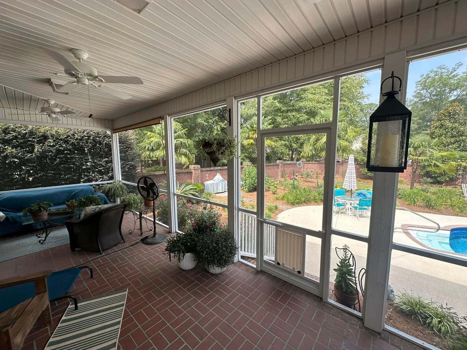 Covered patio with red brick floor, screened windows, lounge chairs, and a pool visible outside.