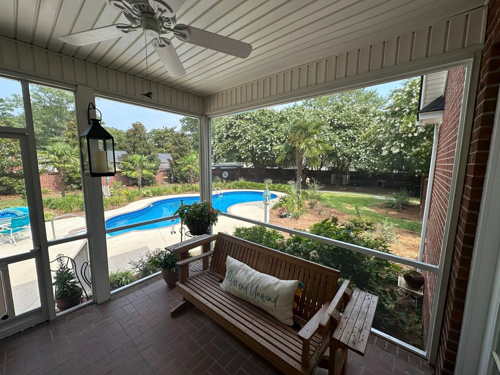 Covered porch with wooden bench overlooking a backyard pool and trees