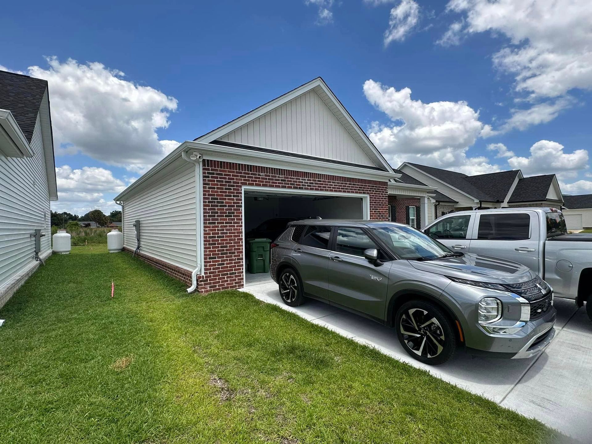 Single-car garage with a dark SUV parked in the driveway of a suburban house under a cloudy blue sky