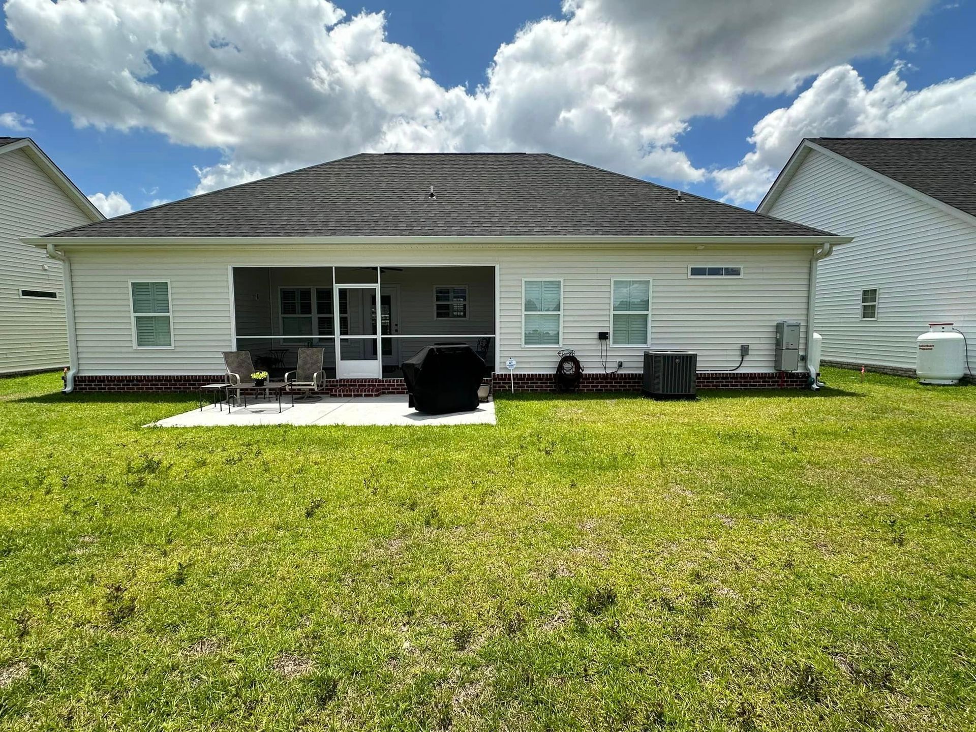Single-story white house with a gray roof, front porch, and lawn under a partly cloudy sky