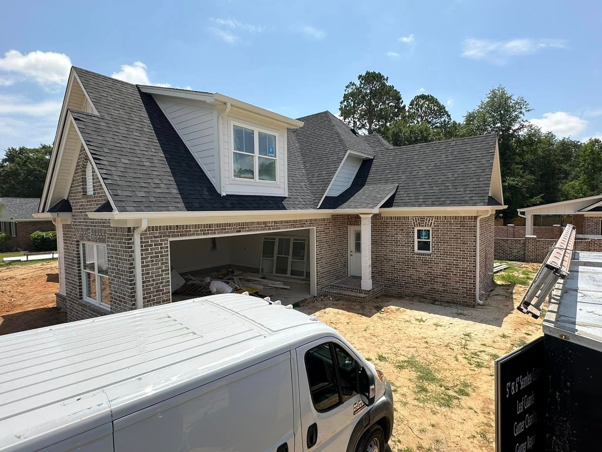 Partly built brick house with dark roof and a white van in the foreground during construction.