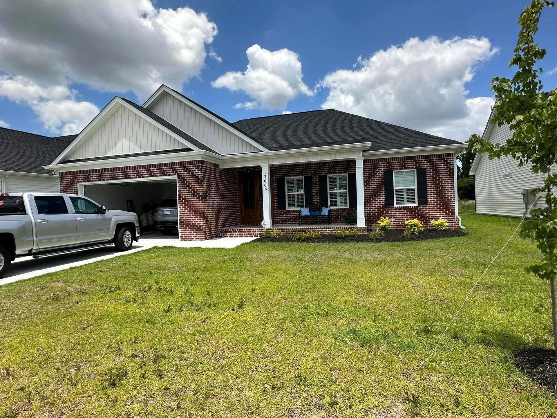 Single-story brick house with a white pickup truck parked in the driveway on a sunny day.