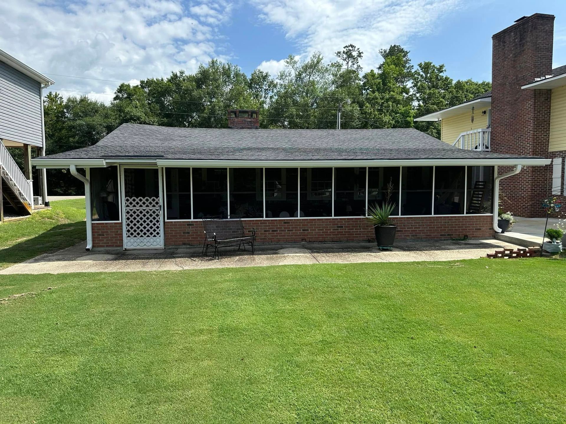 Single-story brick house with a screened porch, chimney, and large green lawn.