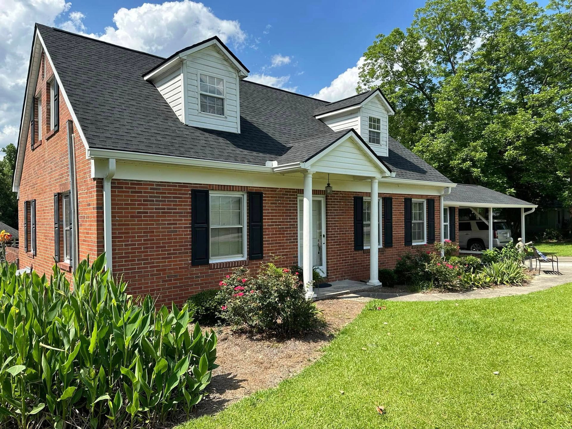 Brick house with white trim and front porch, surrounded by greenery under a bright blue sky
