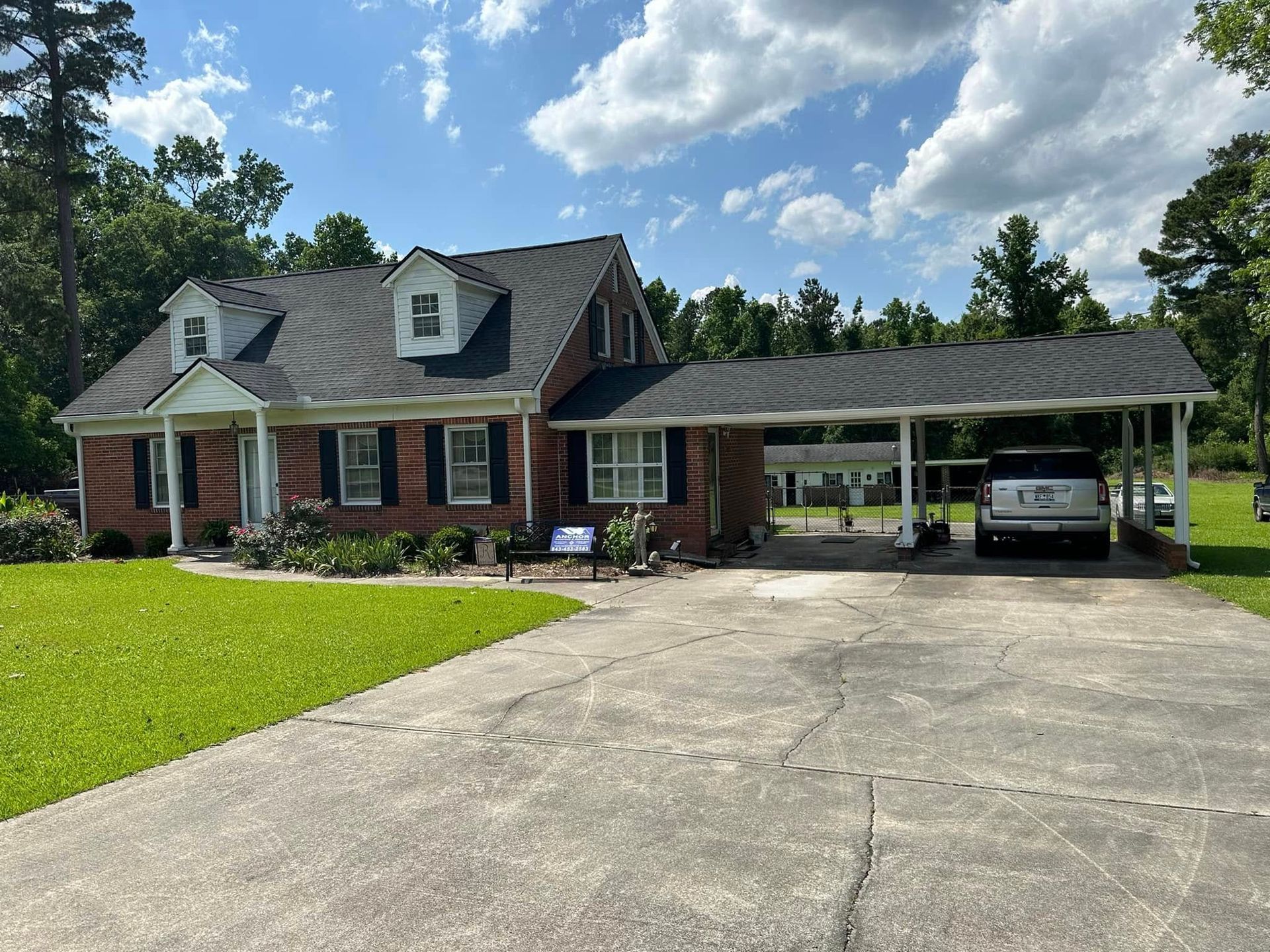 Brick house with white trim and carport, long driveway, and a white SUV under the roof.