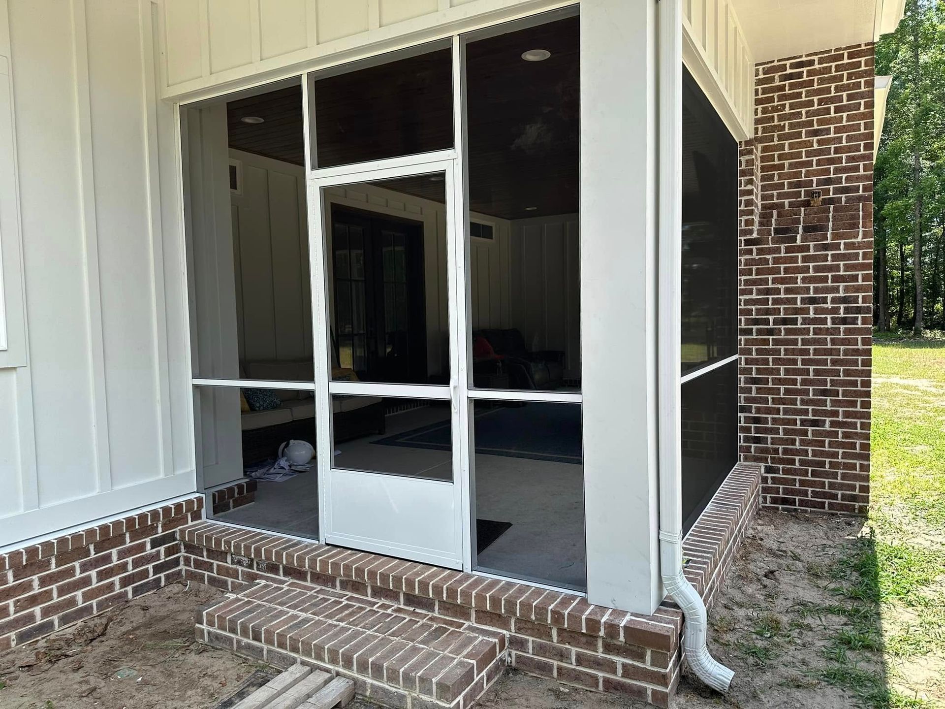 Screened porch with brick steps, white siding, and a black-framed glass door or window.