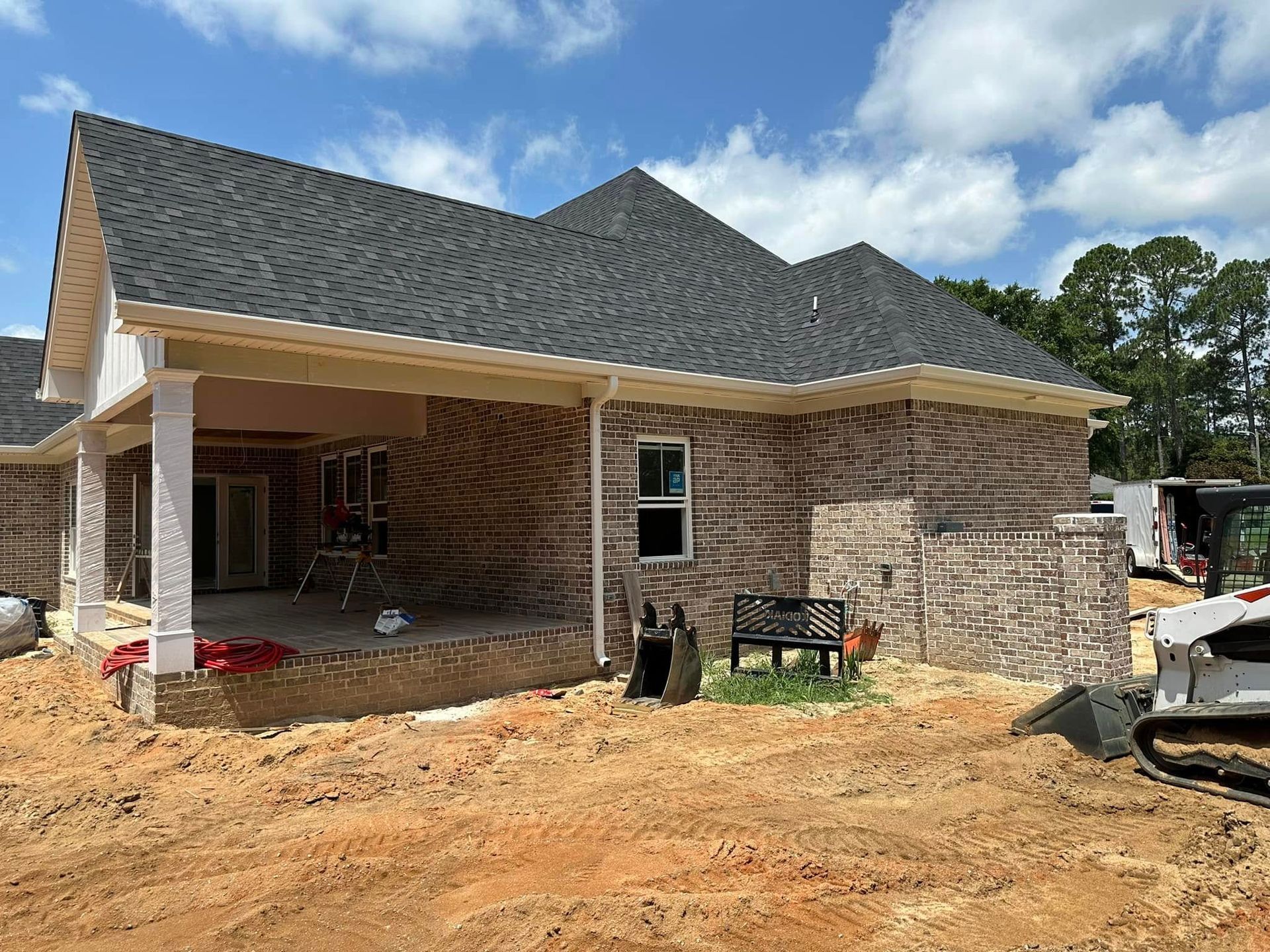 Partially built brick house with a covered porch and dark shingle roof on a dirt lot