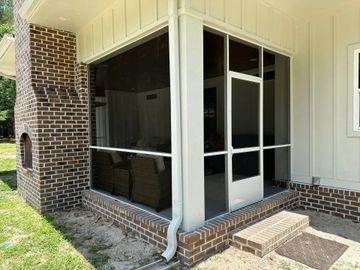 Screened porch corner with white trim, brick base, and a black mesh enclosure beside a house exterior.