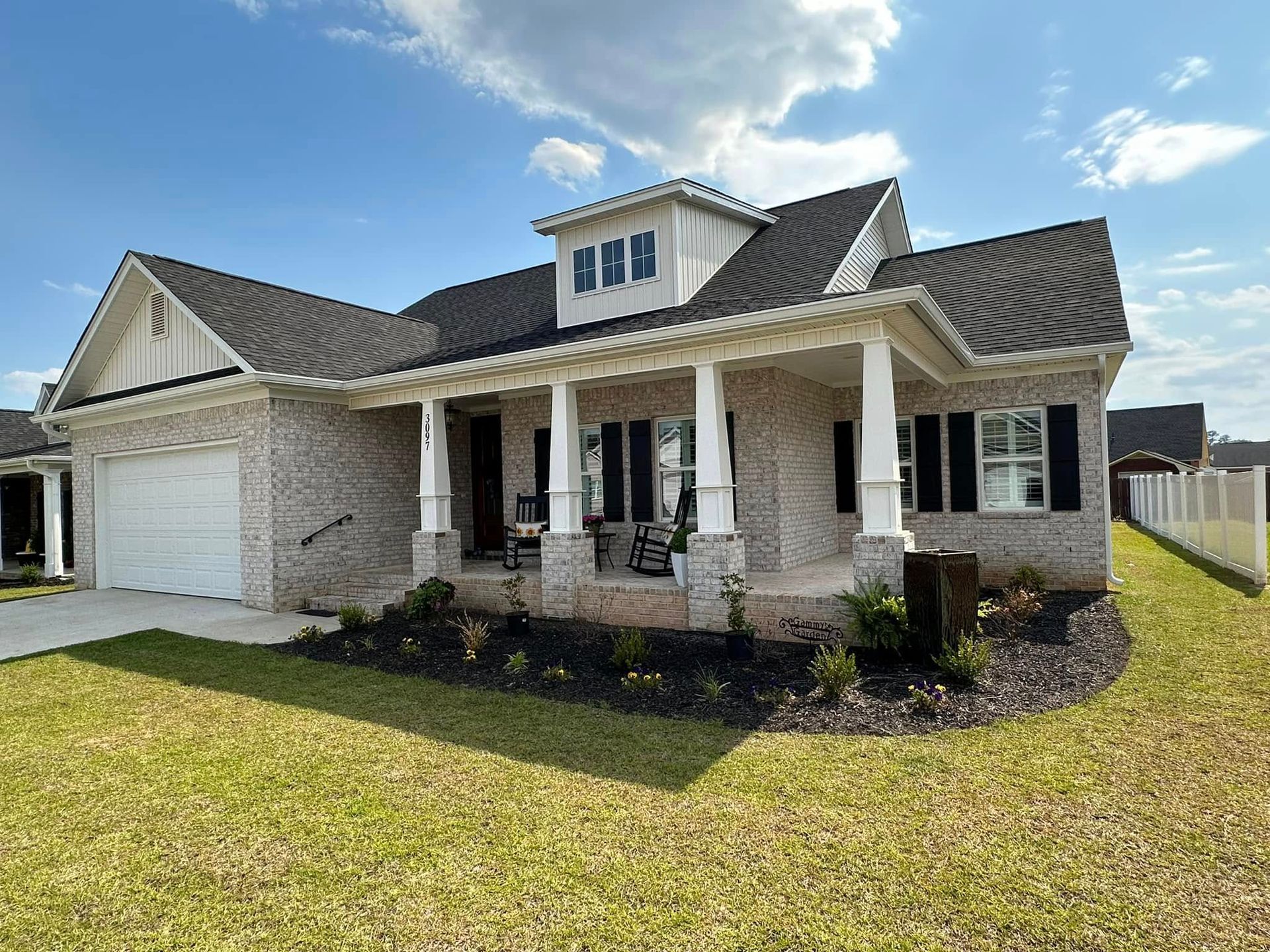 Single-story brick house with white columns, garage, and manicured lawn under a blue sky