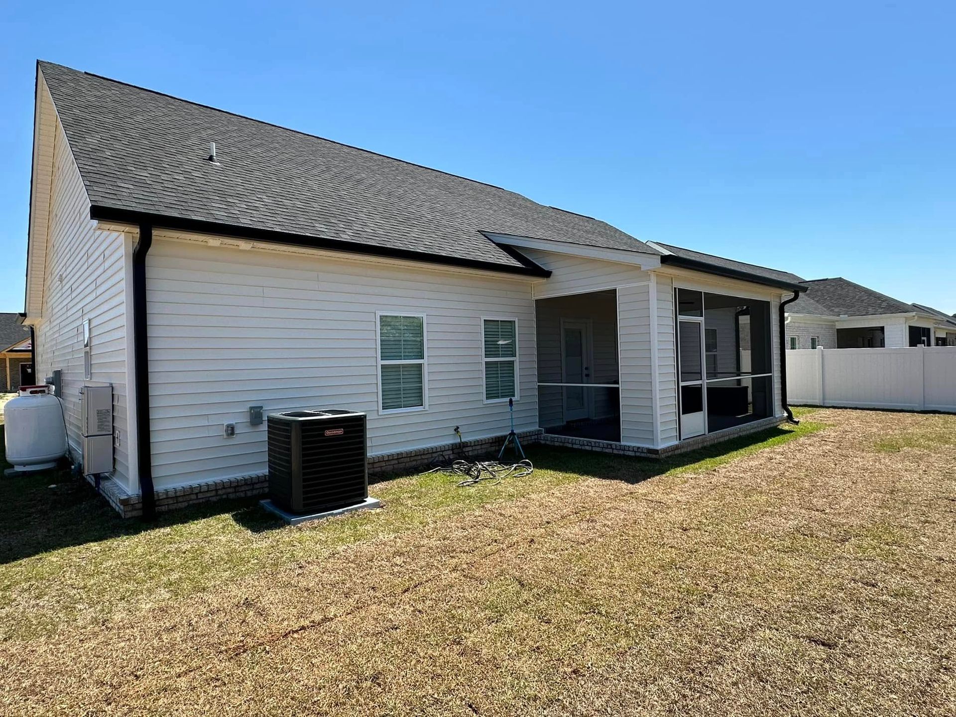 Backyard view of a white house with a screened porch and air conditioner unit under a blue sky