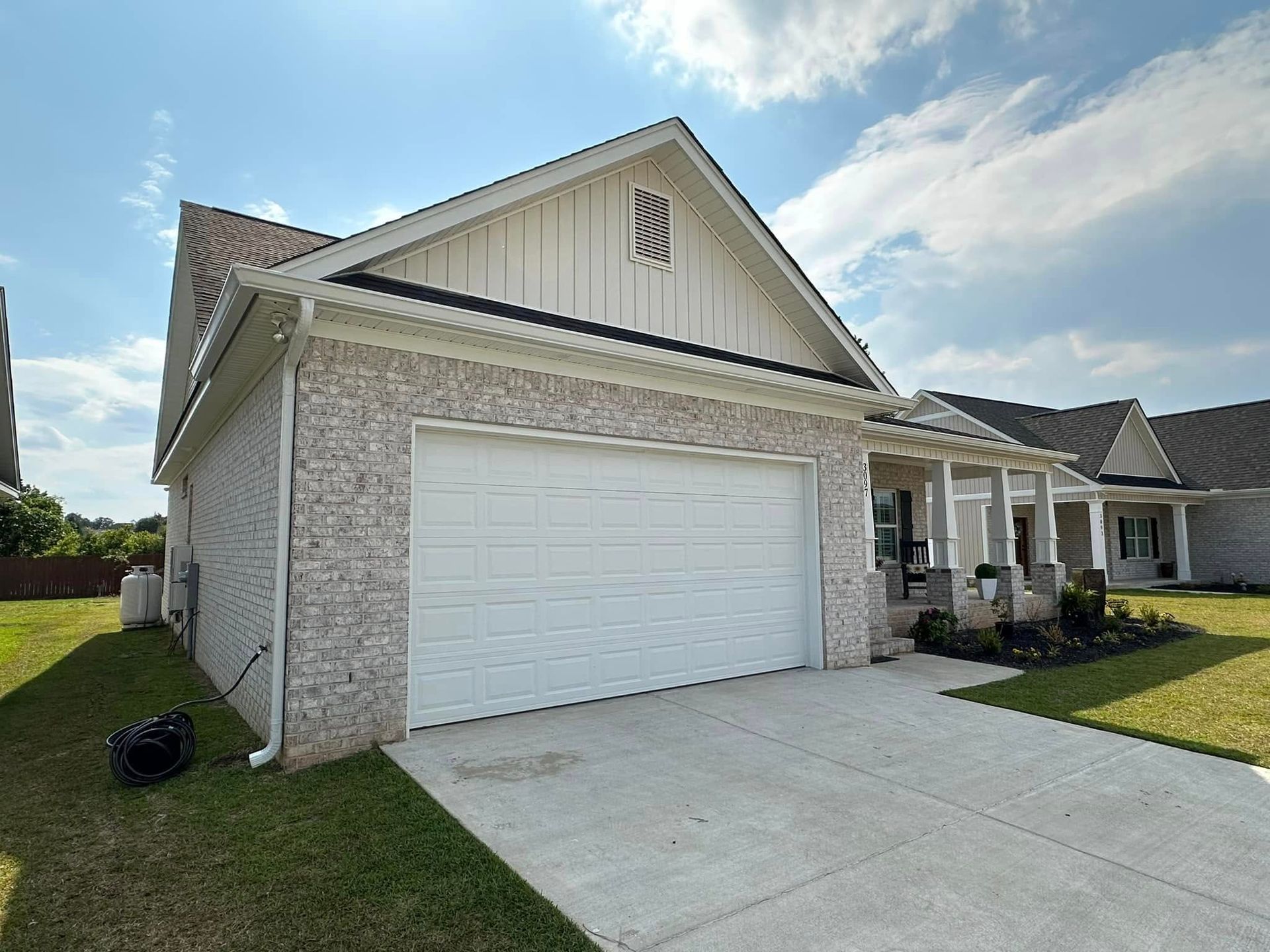 Suburban home exterior with white garage door, brick siding, and a concrete driveway under a partly cloudy sky
