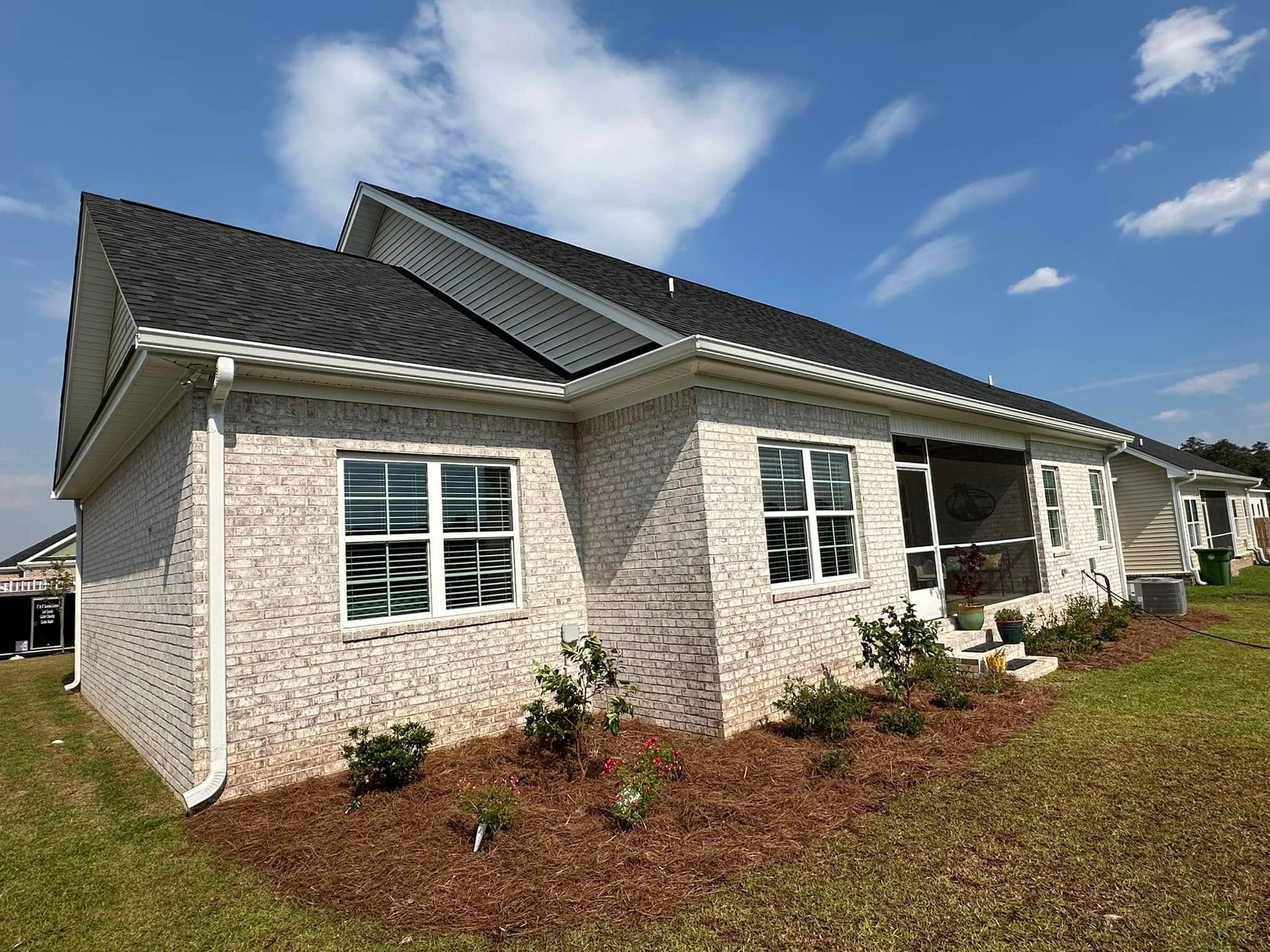 Modern white brick house with dark roof, front windows, and landscaped yard under a blue sky