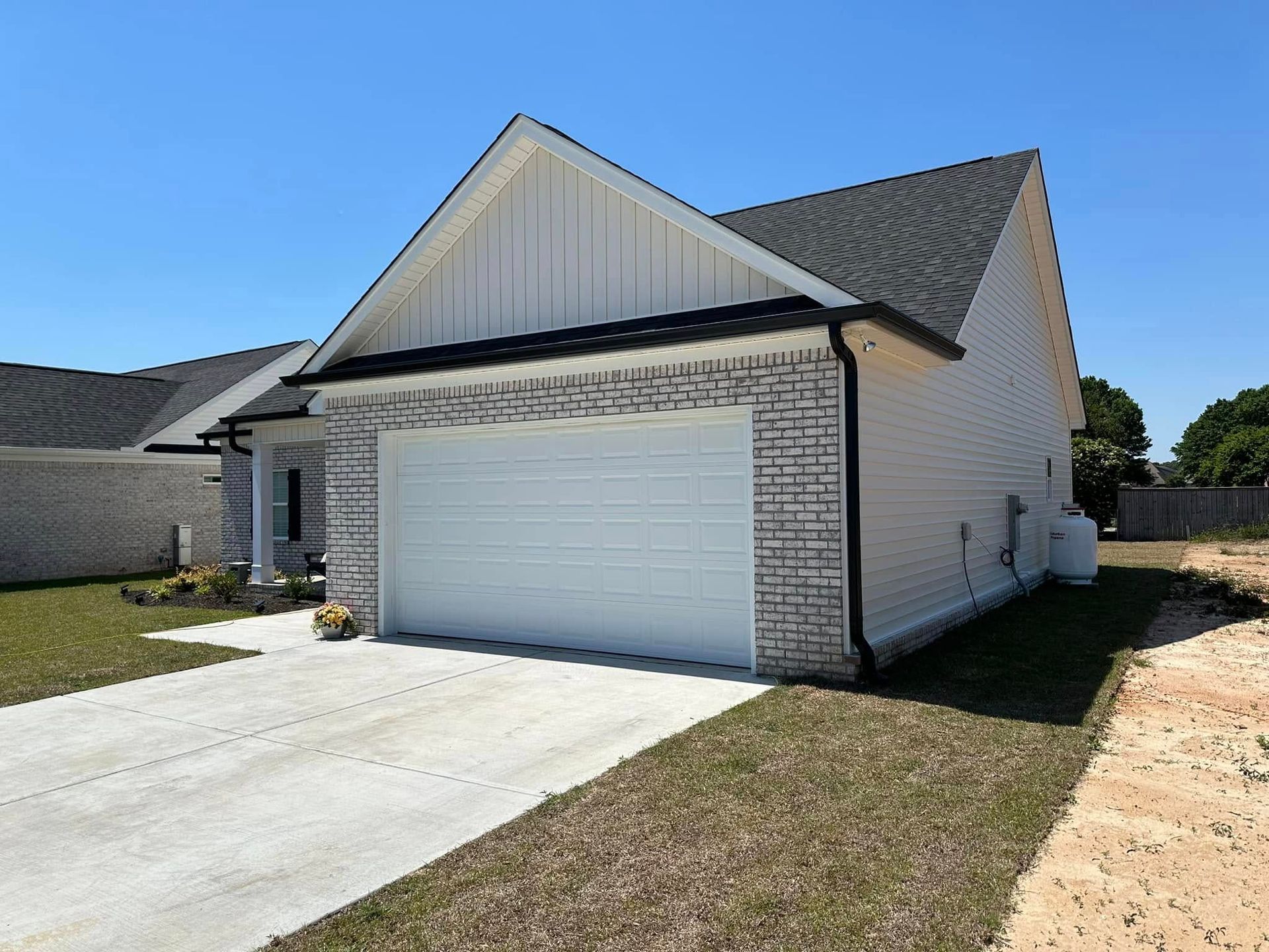 Suburban house with white garage door, brick accents, and a concrete driveway under a clear blue sky