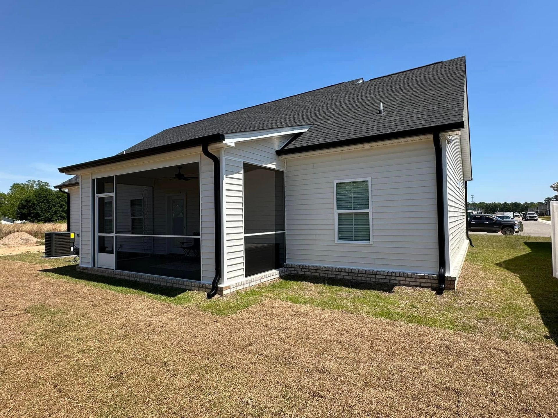 Small white house with black roof and front porch on a grassy lot under a clear blue sky