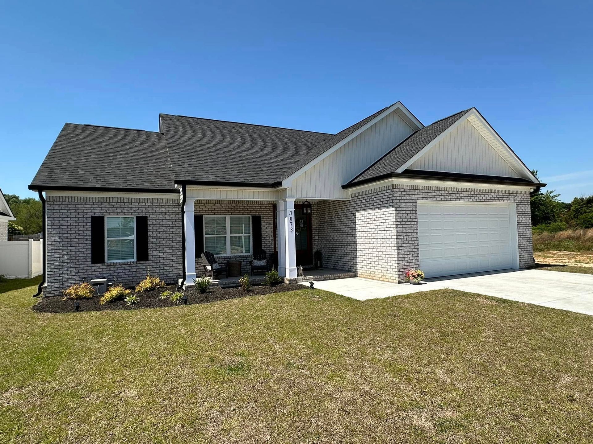 Single-story gray brick house with a two-car garage and front lawn under a clear blue sky