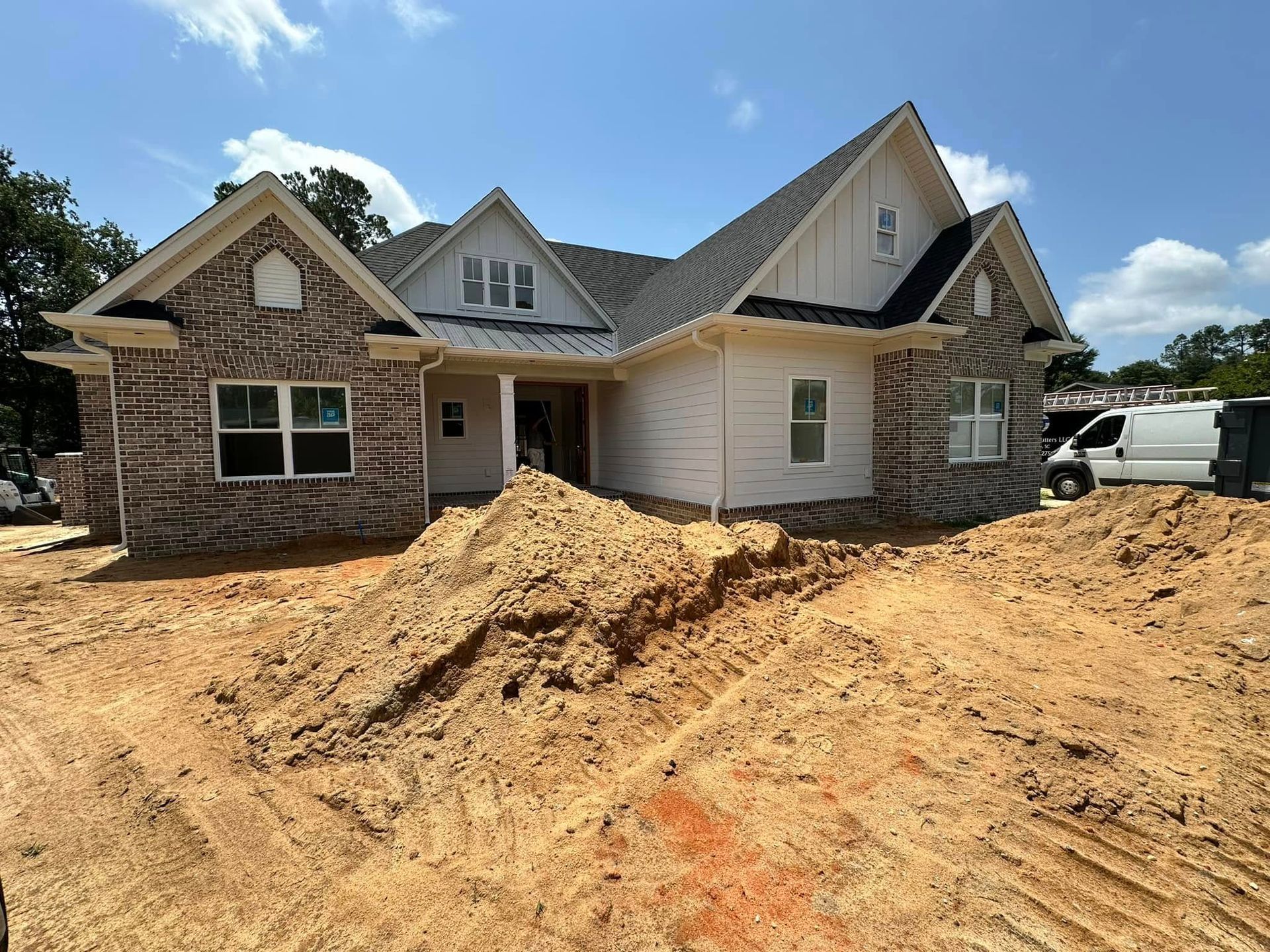 Partially built house with dirt piles and a white truck under a blue sky