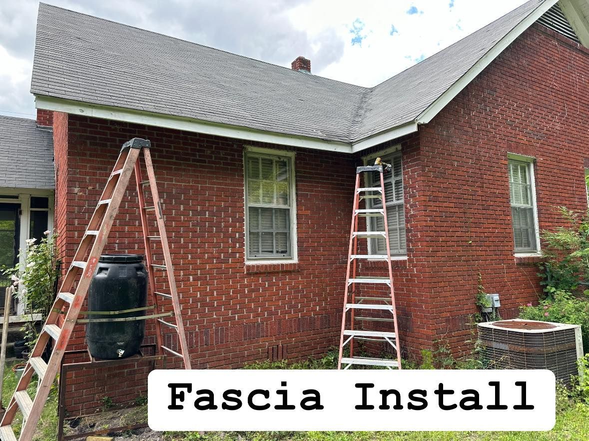 Workers on ladders installing fascia on a red brick house with a gray roof