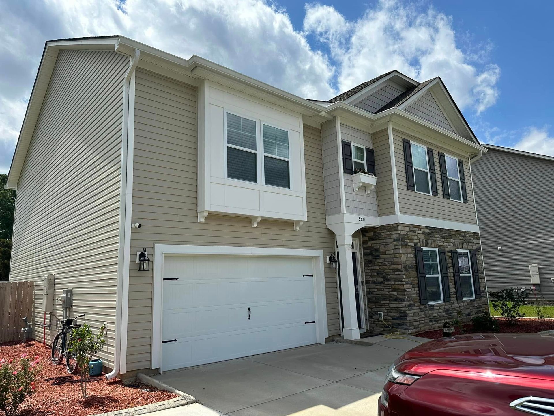 Two-story beige house with white trim, garage, and stone entry under a partly cloudy sky