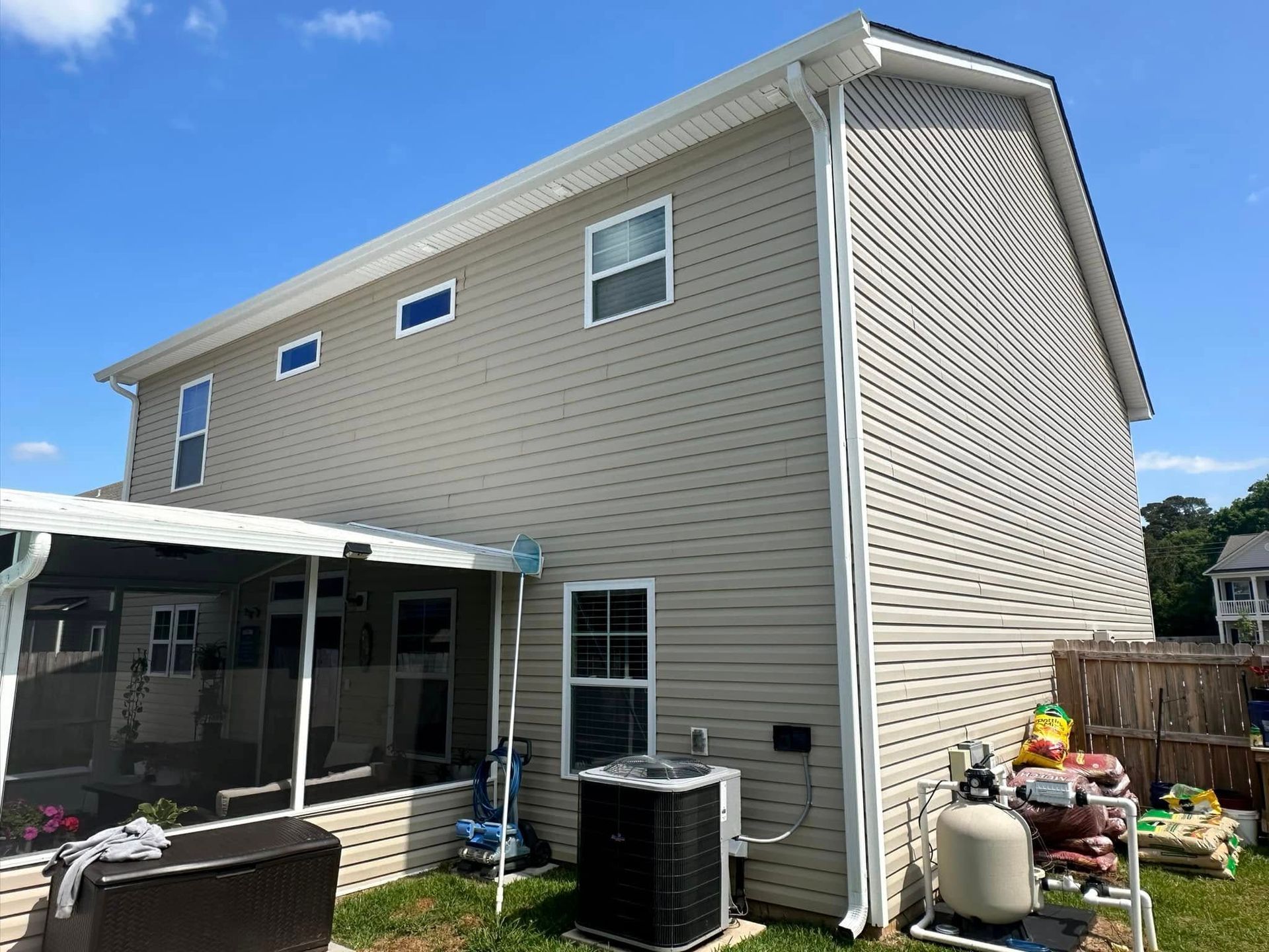 Backyard view of a beige two-story house with screened patio and outdoor AC units