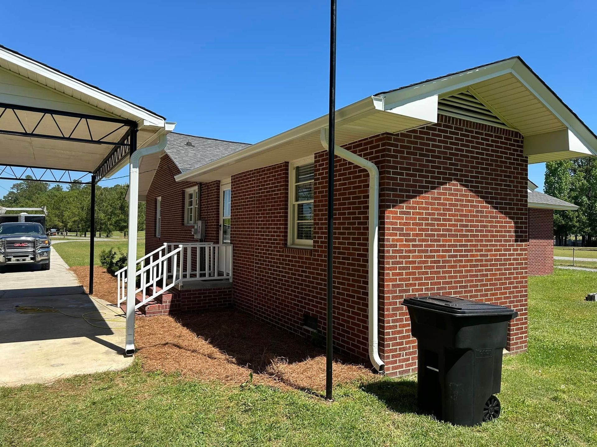 Small brick building with white trim and porch ramp beside a carport, on a grassy lot.
