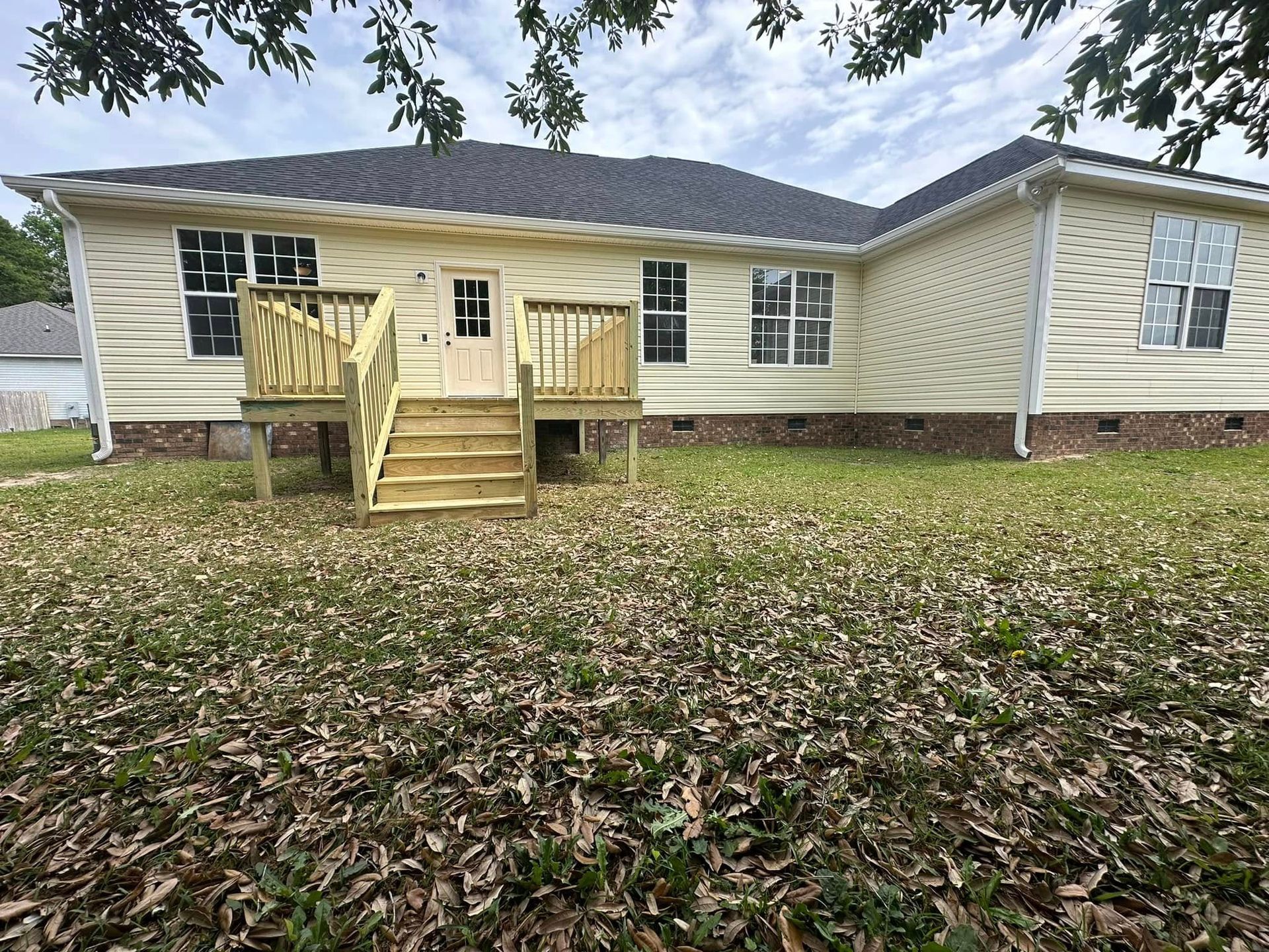 Single-story beige house with a small front porch, steps, and leaf-covered yard.