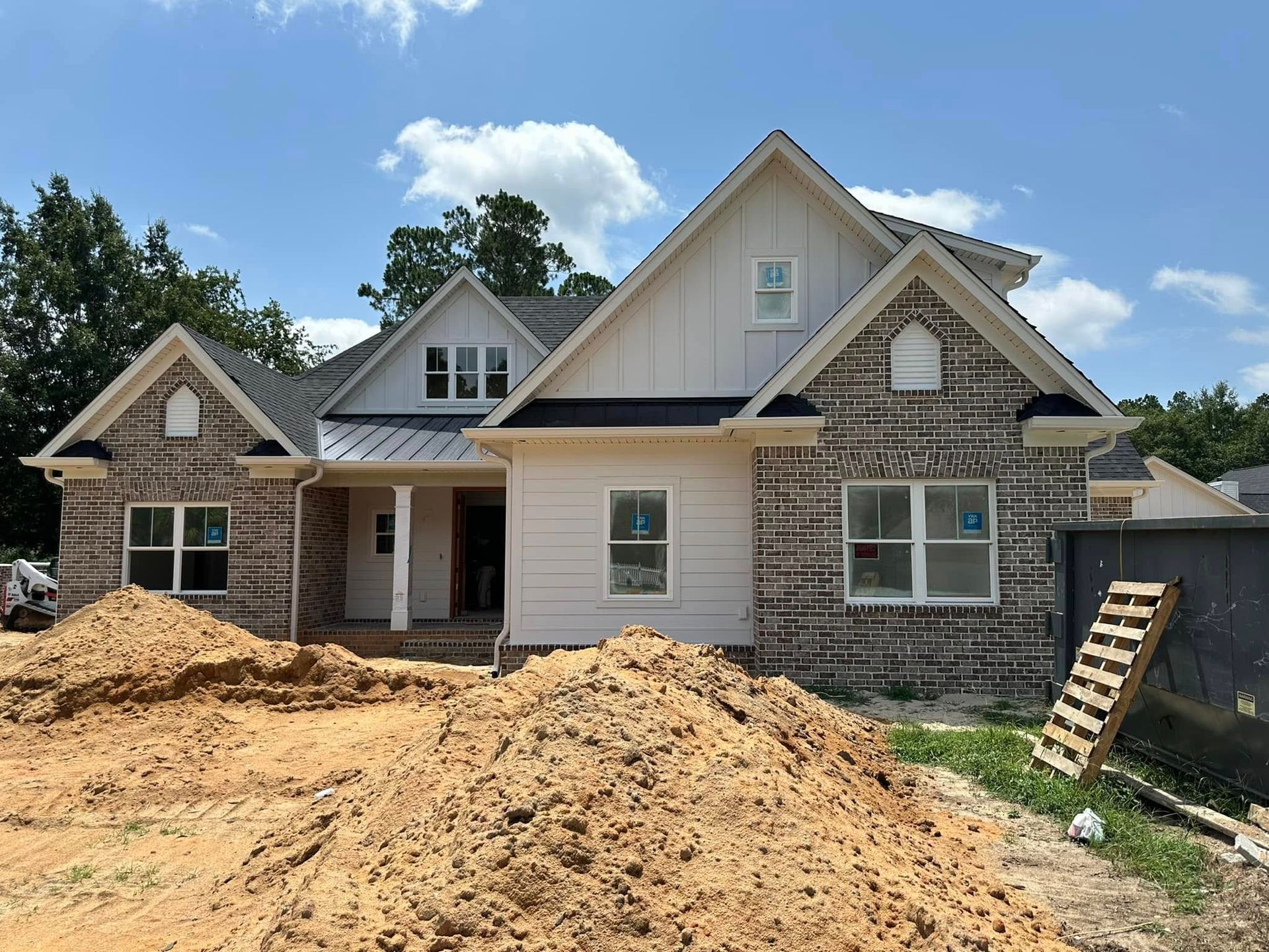 New house under construction with stone facade, wood siding, and piles of dirt in front