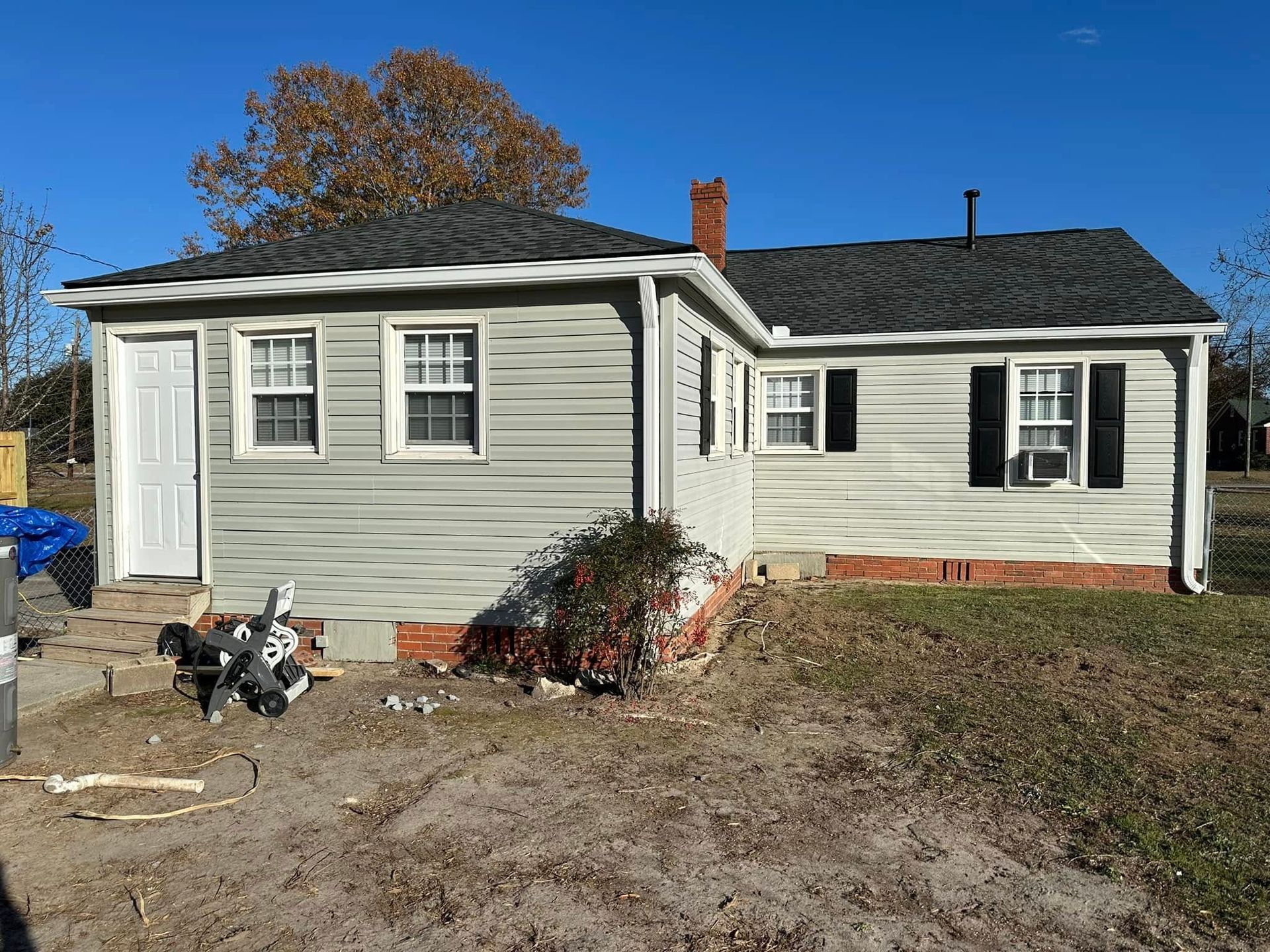 Small white house with black shutters, a front yard, and a parked motorcycle under a blue sky.