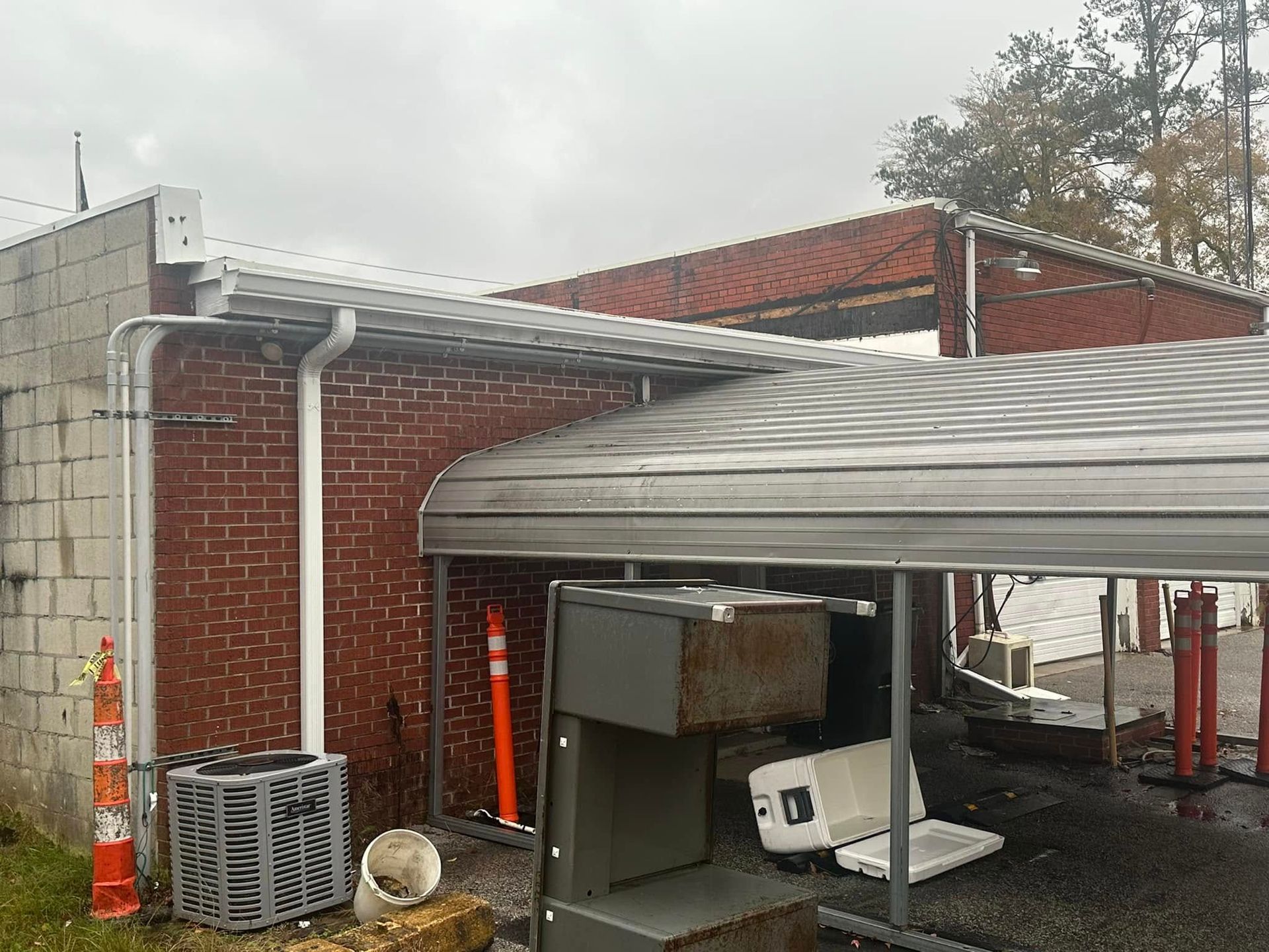 Construction area beside a brick building with scaffolding, guttering, and a red-tiled roof under a gray sky