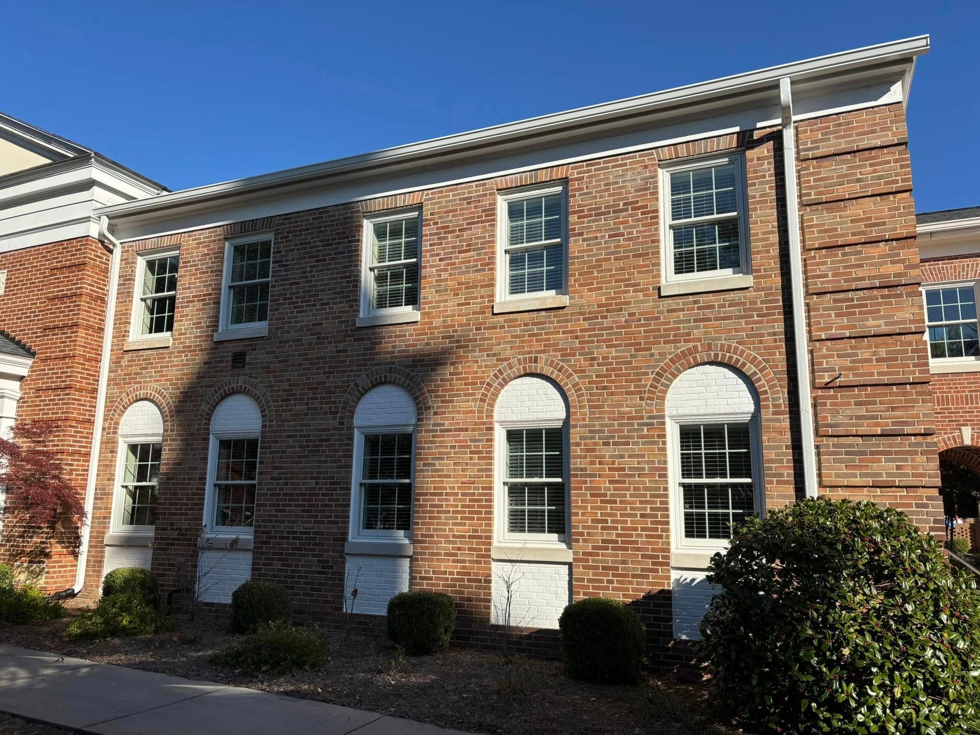 Brick townhouse with white trim and arched windows in bright sunlight