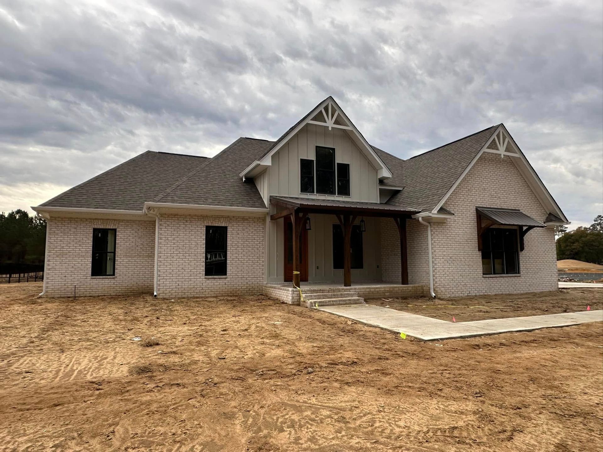 Newly built beige house with gray roof and unfinished dirt yard under cloudy sky