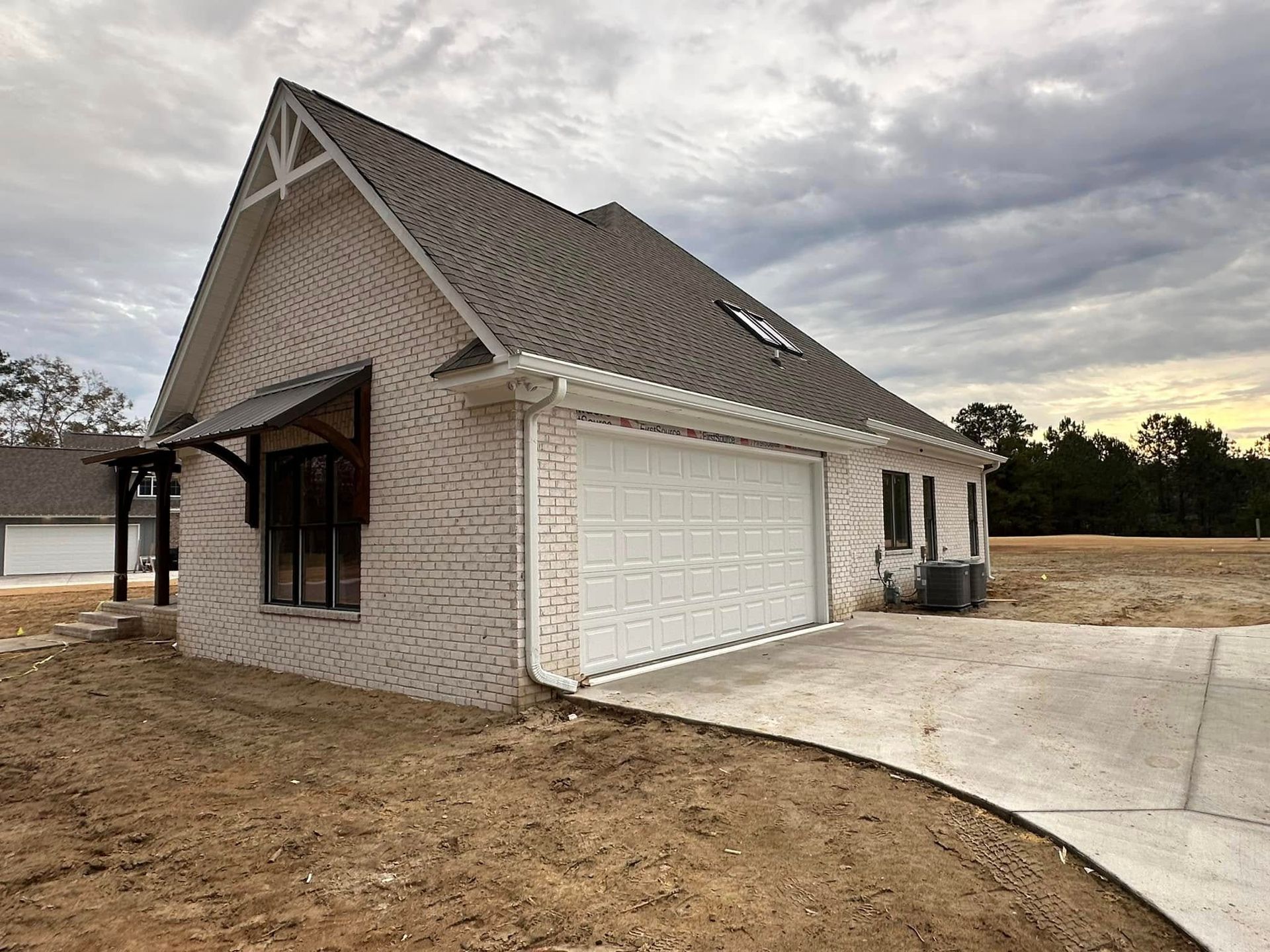 New brick house with a gabled roof and double garage beside a curved driveway under cloudy skies