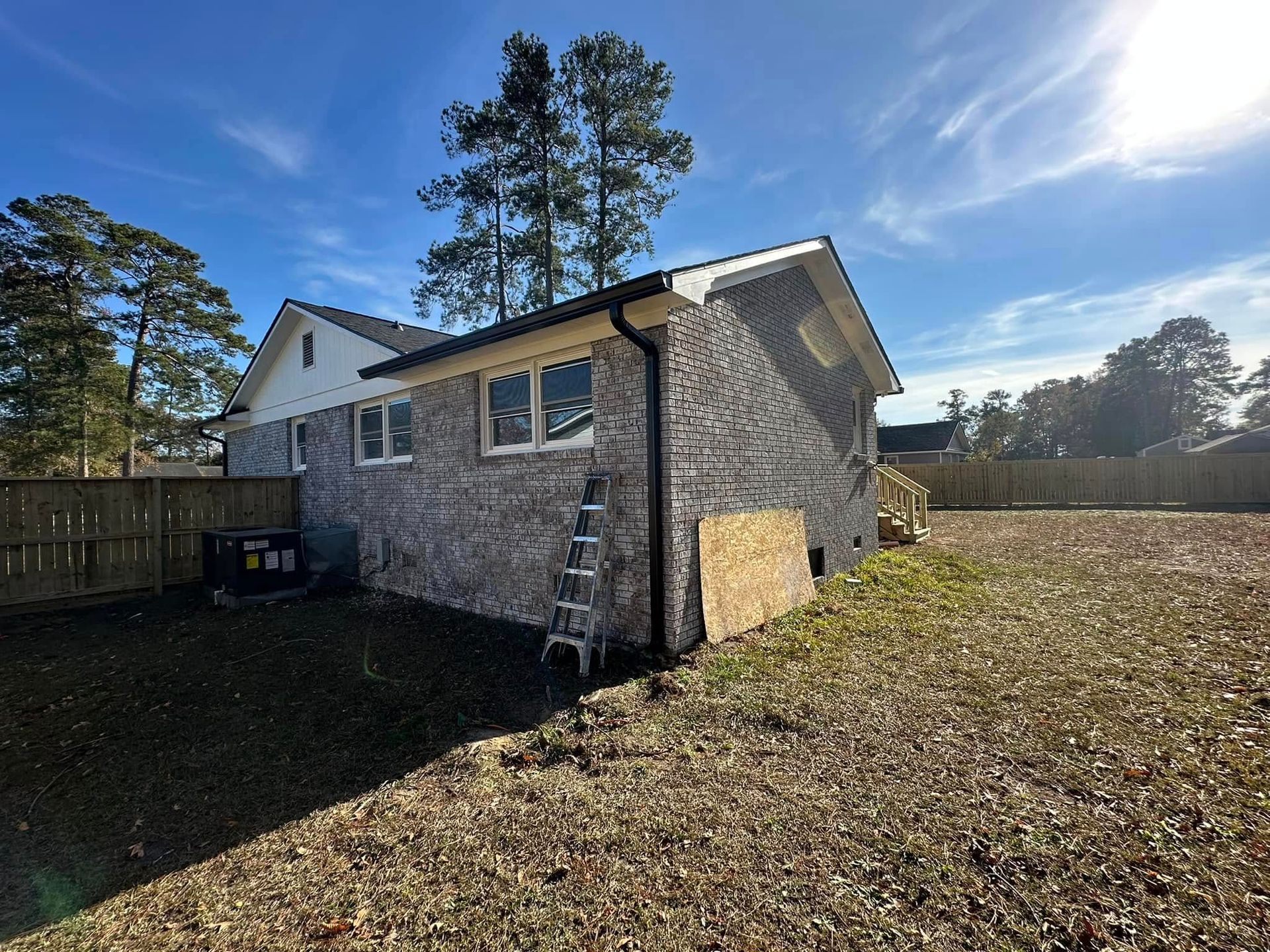 Stone house addition with small windows and ladder, set in a sunny fenced backyard