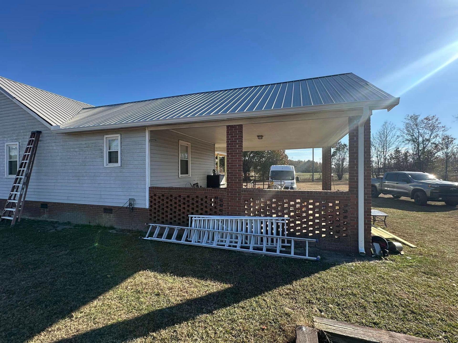 Brick house porch with metal roof, ladder leaning on side, and ladder sections stacked on the ground