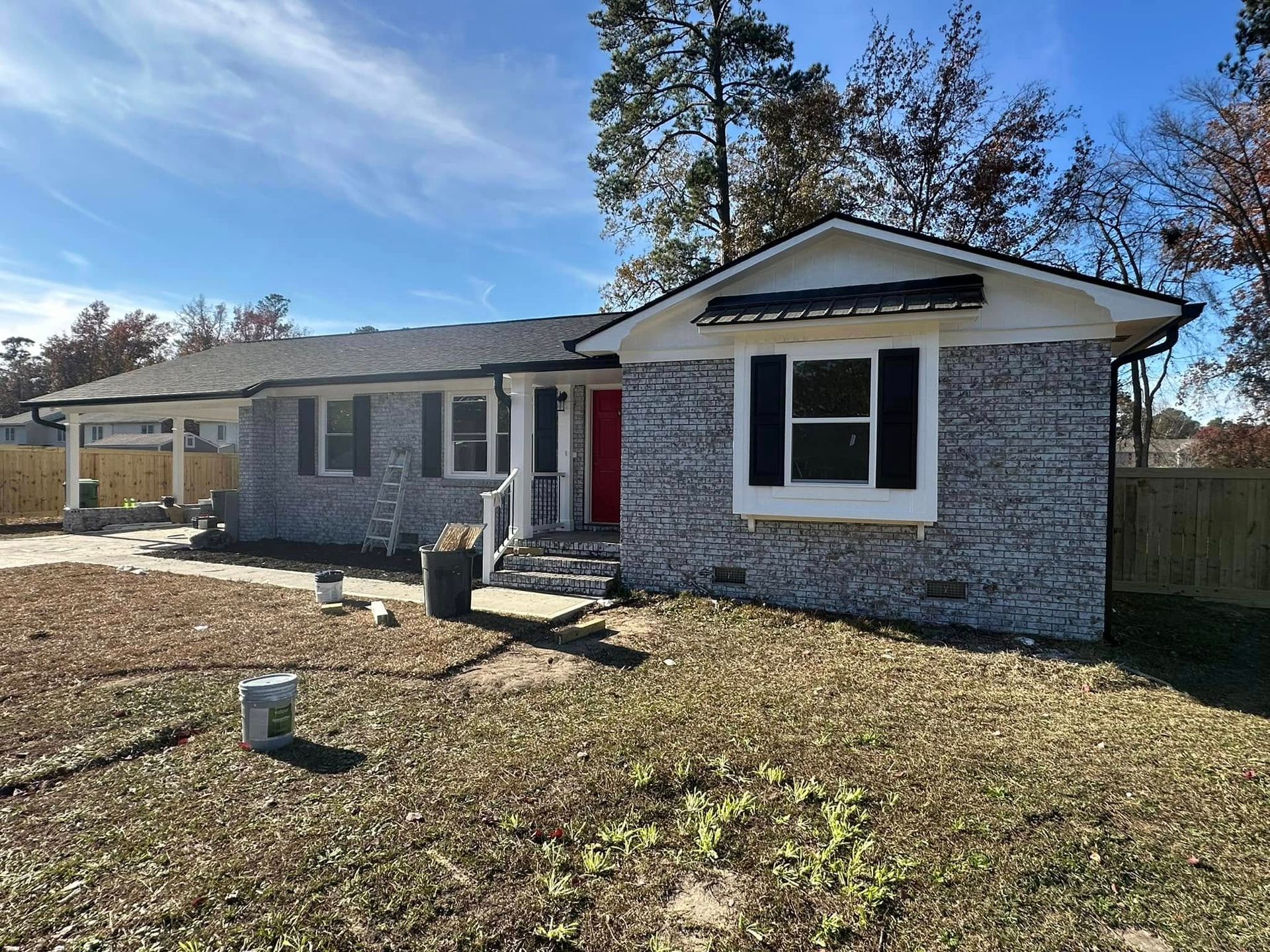 Single-story house with gray siding, red front door, and a front yard under a clear blue sky
