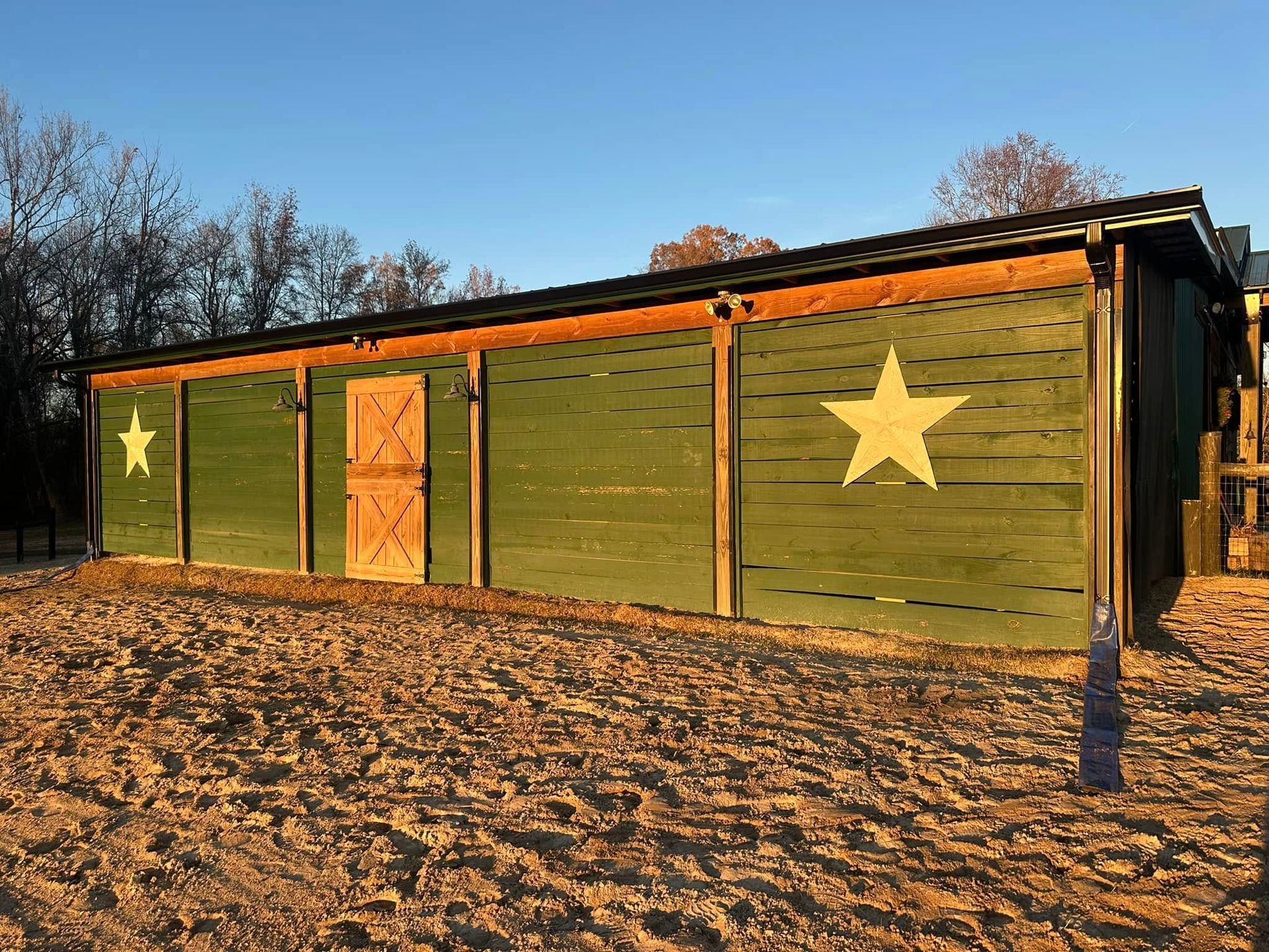 Green shed with large yellow stars on the side, set in a sandy outdoor area at sunset