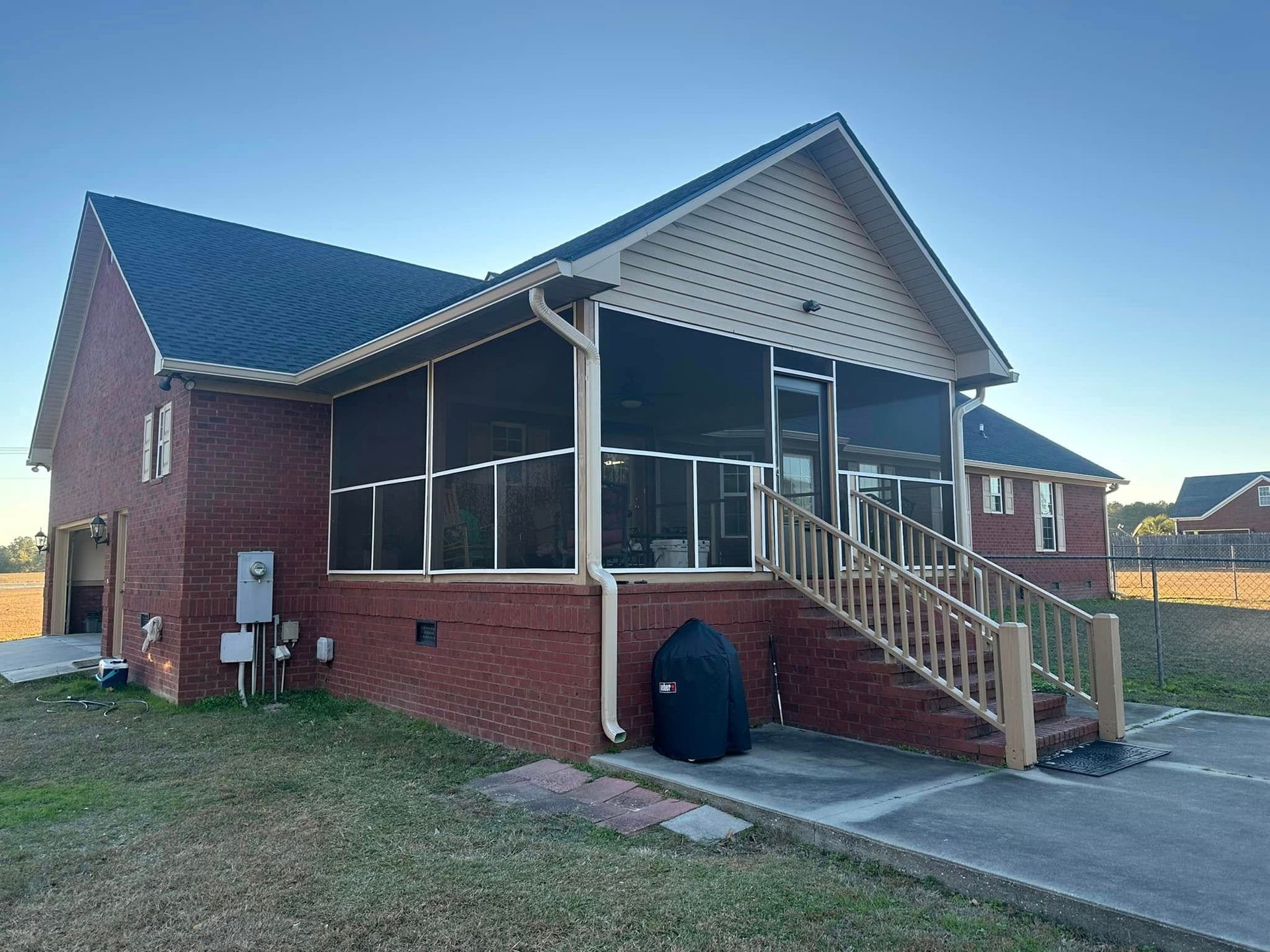 Brick house with a screened porch, front steps, and a grassy yard under a clear sky