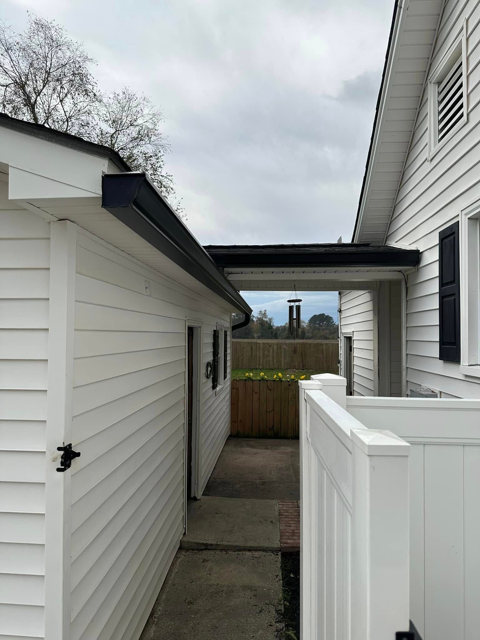 Narrow outdoor passage between white houses with a fence and cloudy sky overhead