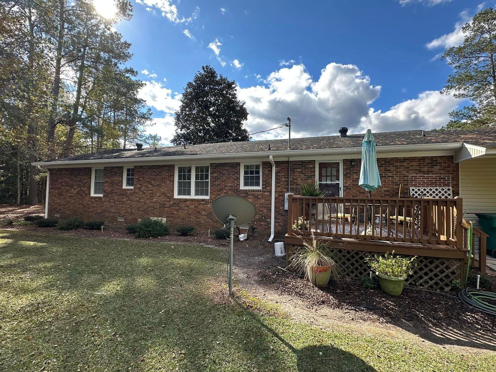 Single-story brick house with a wooden porch, trees, and a grassy front yard under a blue sky.