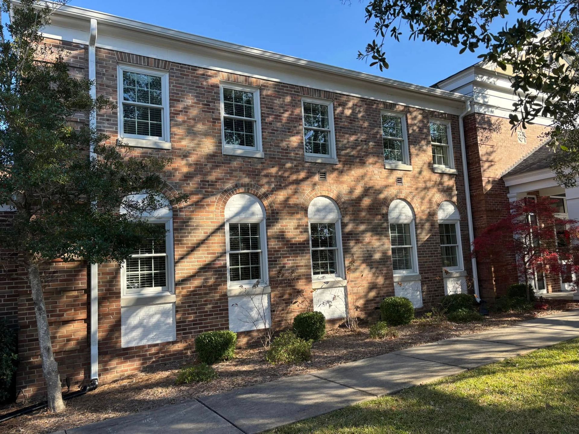 Brick building with white-trimmed windows, a front walkway, and trees casting shade
