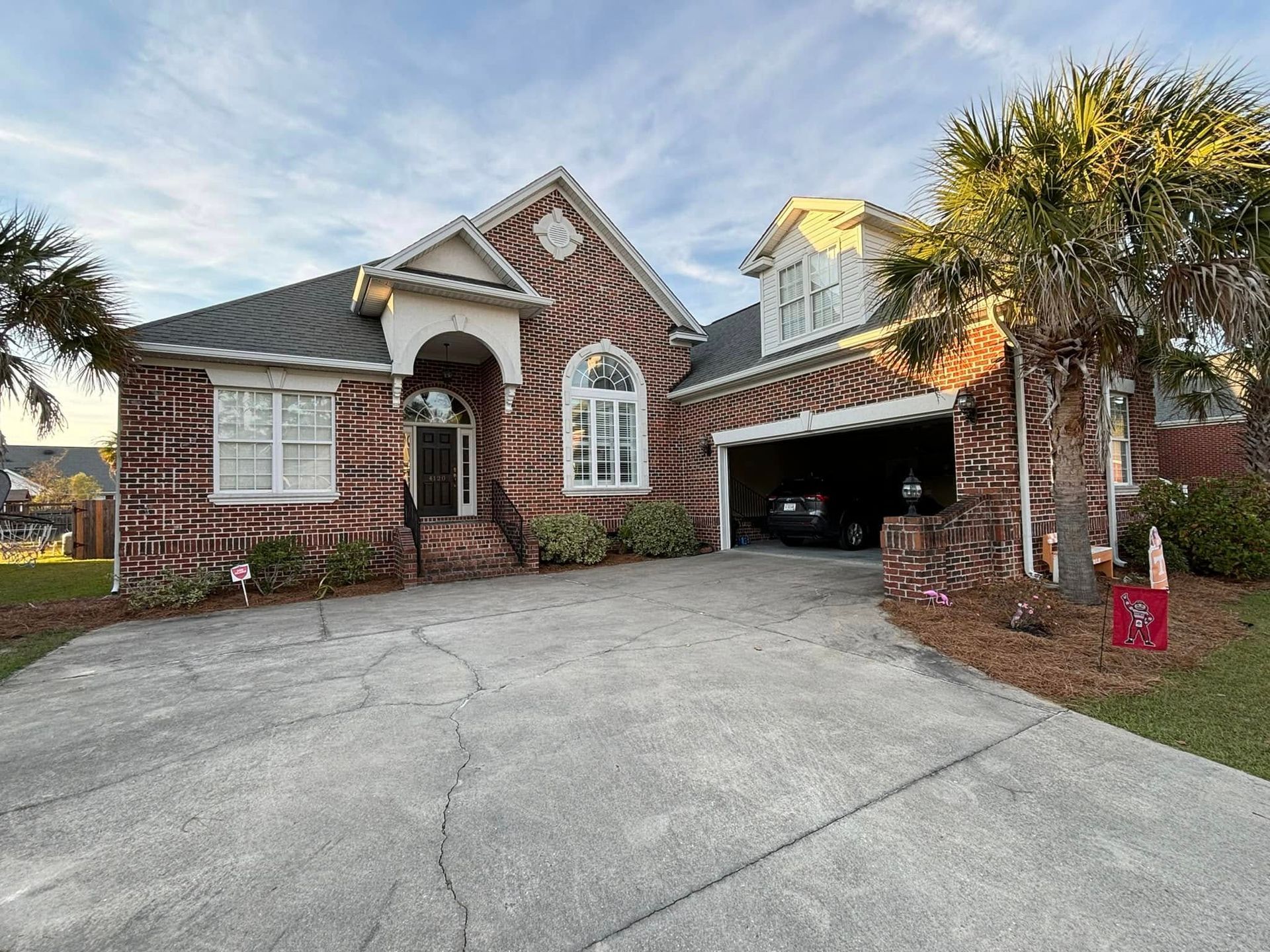 Brick suburban house with arched entry, attached garage, and driveway under a partly cloudy sky