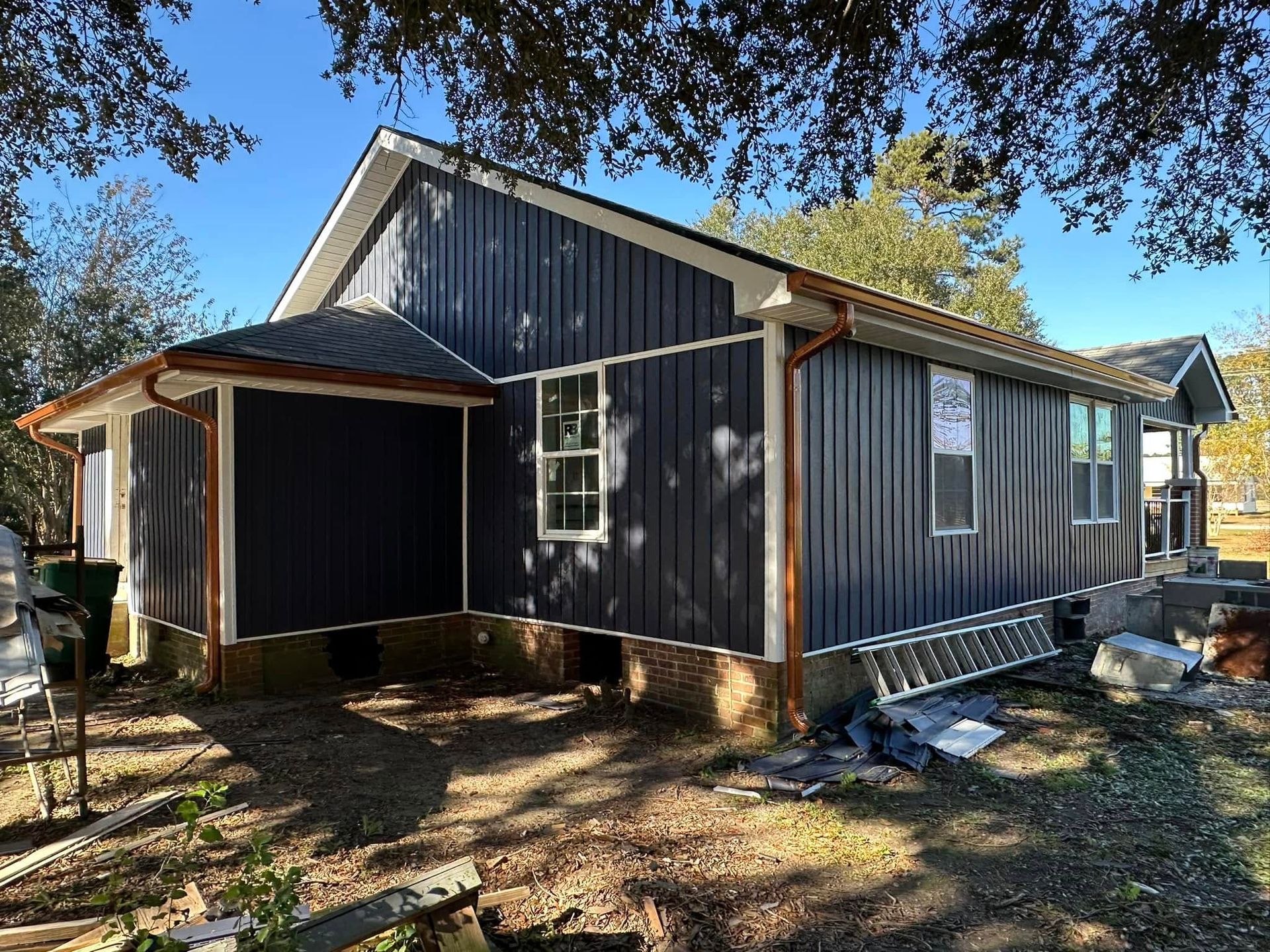 Dark blue house with porch and metal roof on a wooded lot