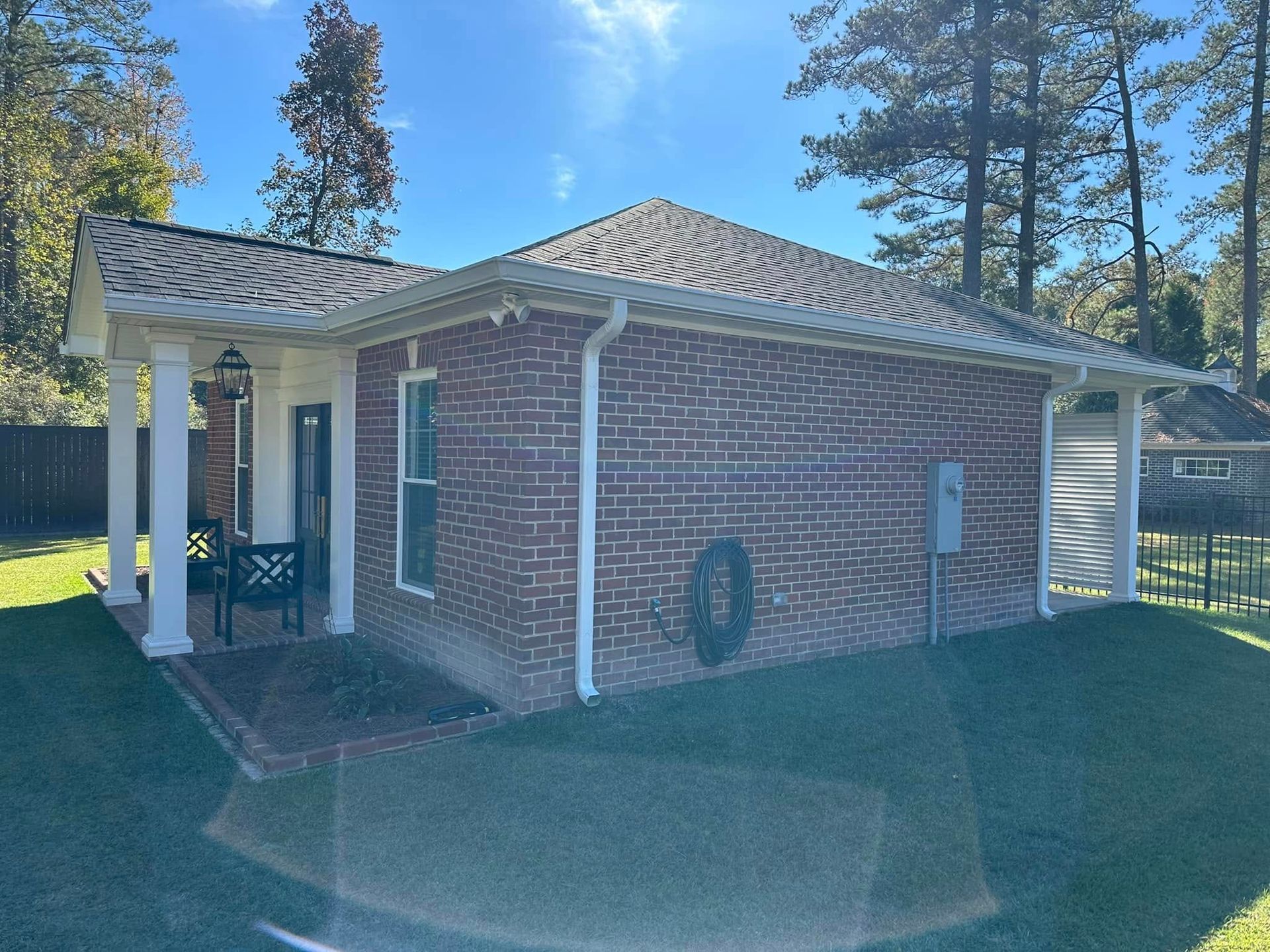 Brick house with white trim and a covered porch in a sunny yard.