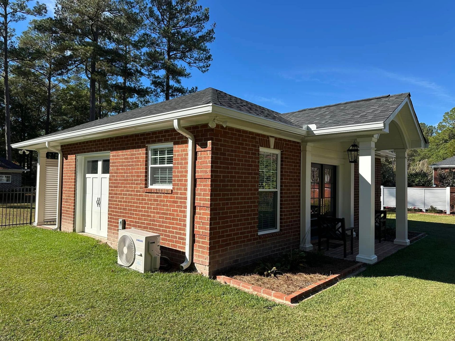 Small red brick house with a white porch and green lawn under a blue sky